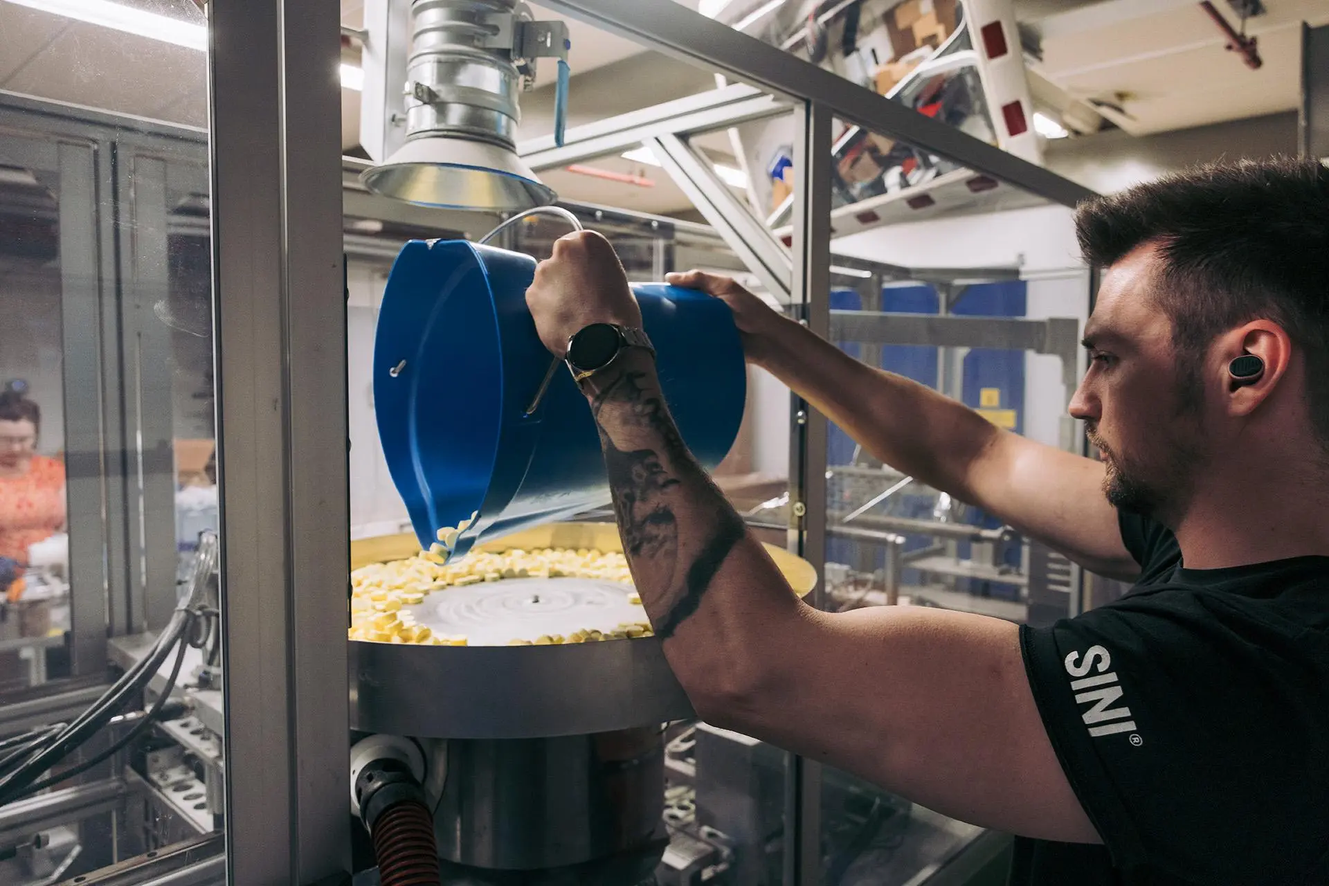 Jere Vihervaara kaataa ämpäristä pieniä puhdistusainepillereitä tehdaskoneeseen.