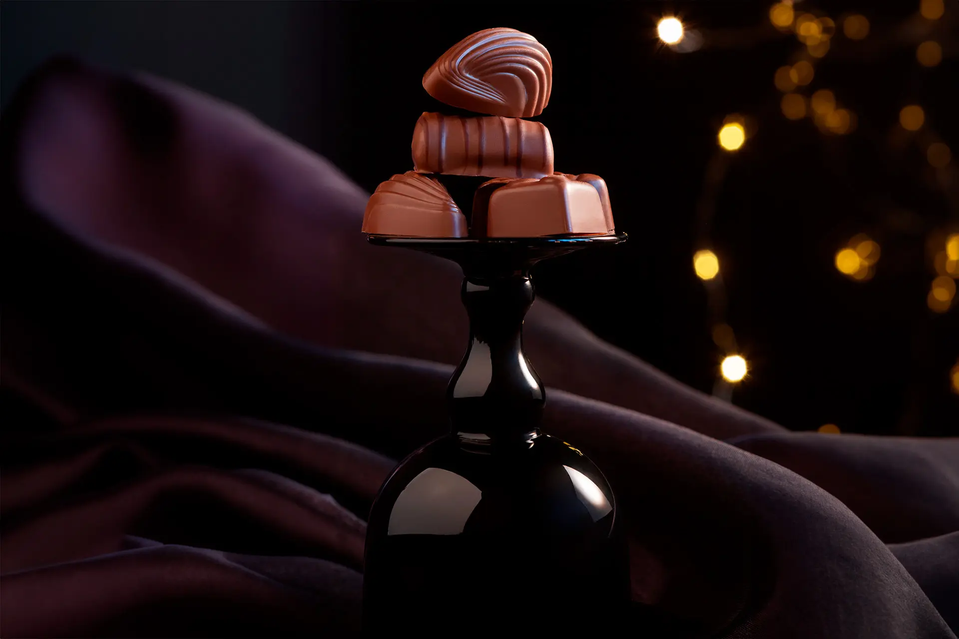Tummataustainen tunnelmallinen kuva, jossa konvehteja mustalla jalustalla.