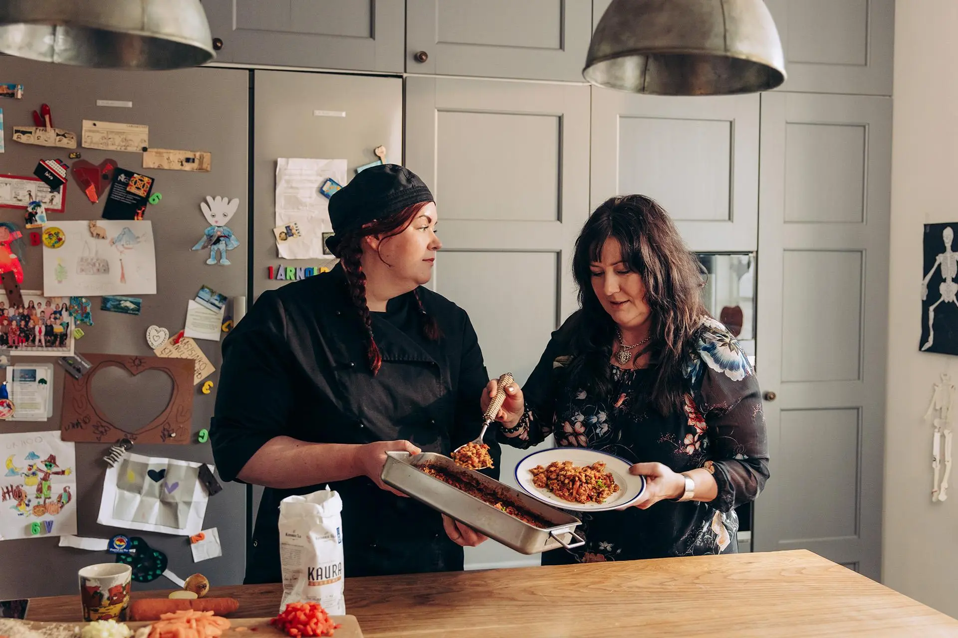 Jenni Turkki pitelee vuokaa, josta Terhi Kinnari ottaa annoksen lautaselle.