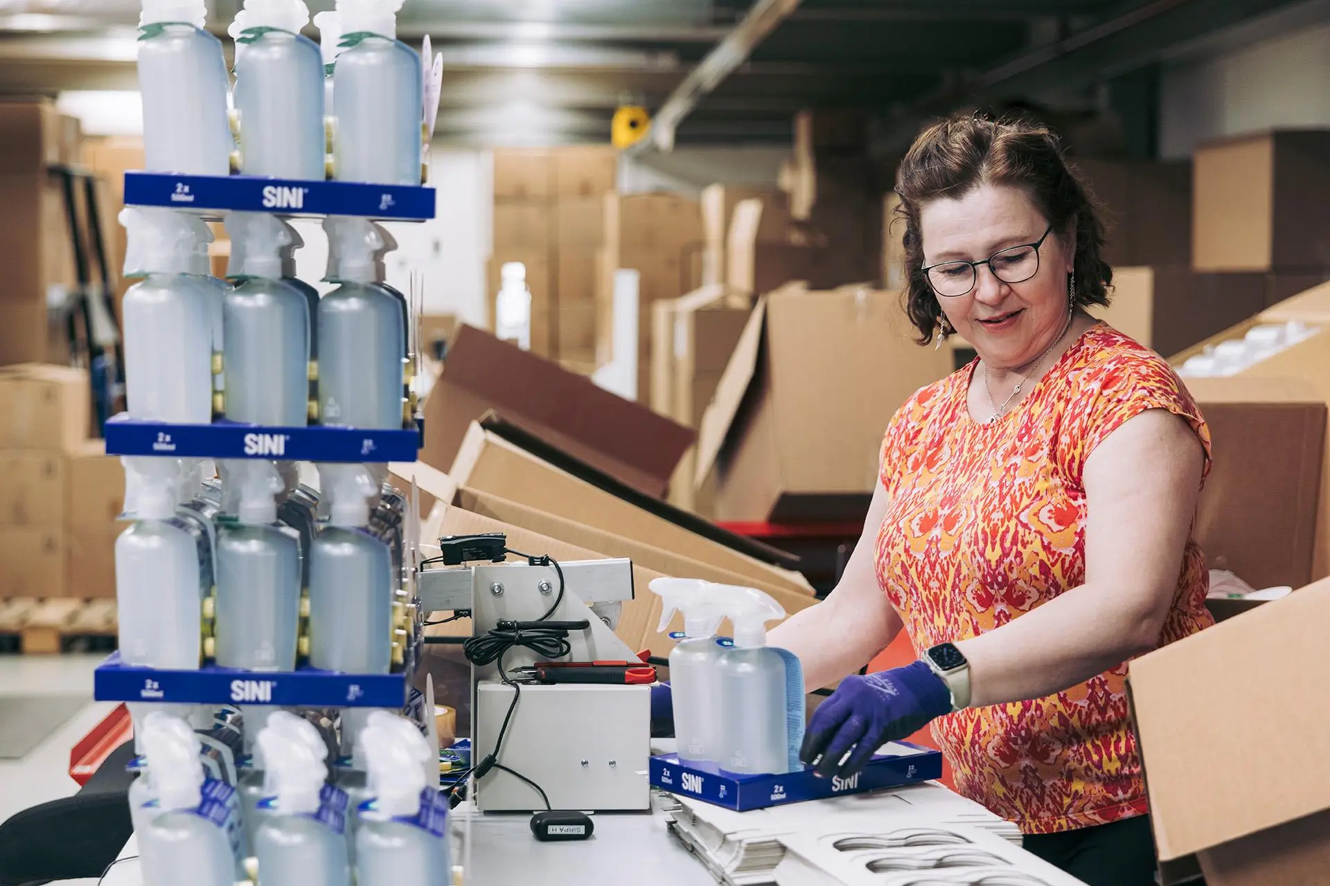 Sirpa Heiska pakkaa Sinituote-suihkepulloja.