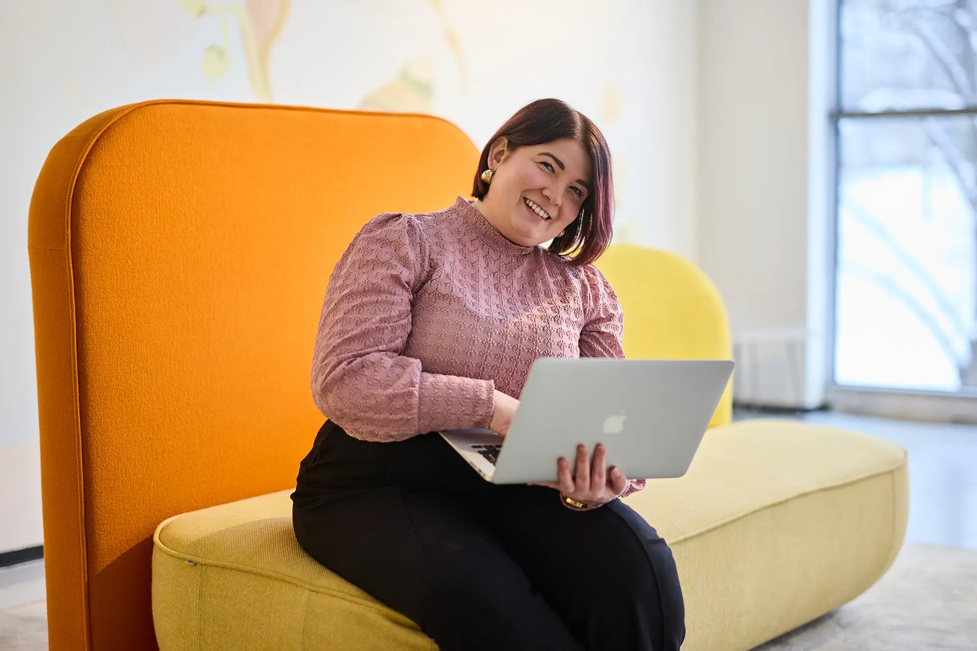 Sasnna Latvala istuu tietokone sylissä kelta-oranssilla sohvalla.