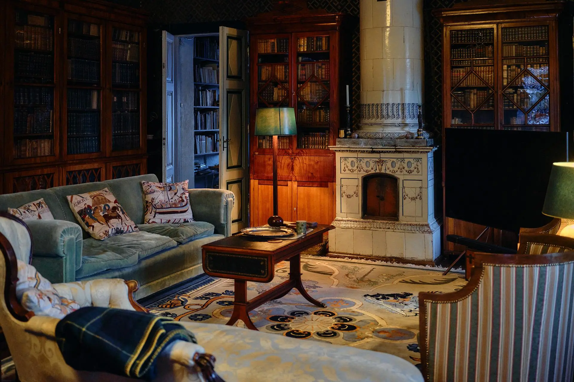 Huone, jossa valkoinen kakluuni, kirjahylly ja vihreä sohva, jossa tyynyjä.