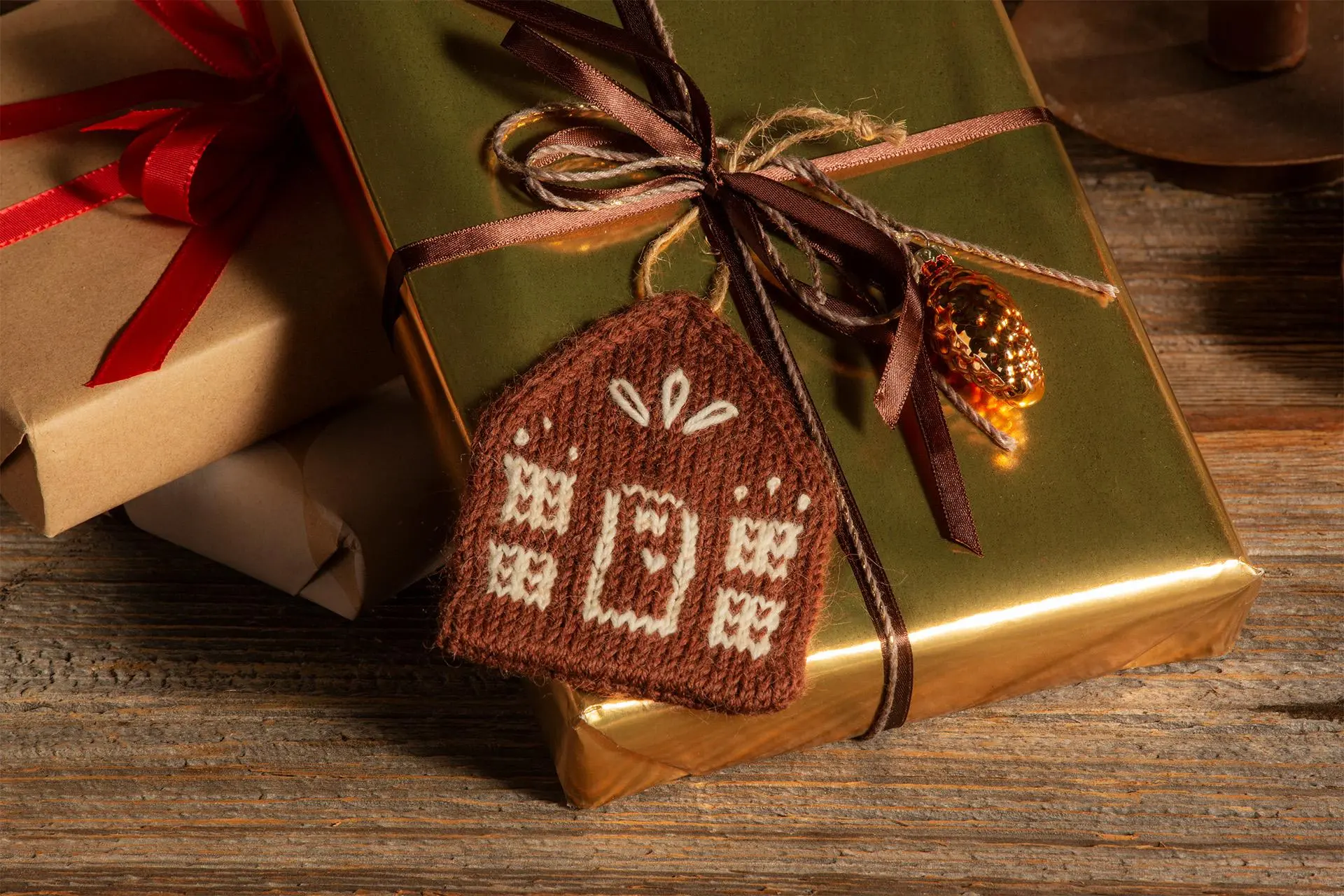 Lahjapakettiin kiinnitetty neulottu joulukoriste, joka näyttää piparkakkutalolta.