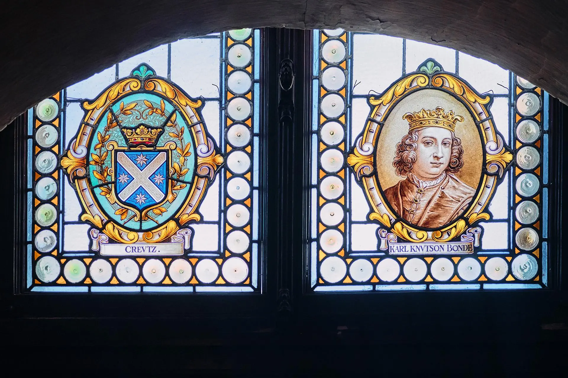 Kaksi ikkunamaalausta: toisessa vaakuna, toisessa miehen kuva.