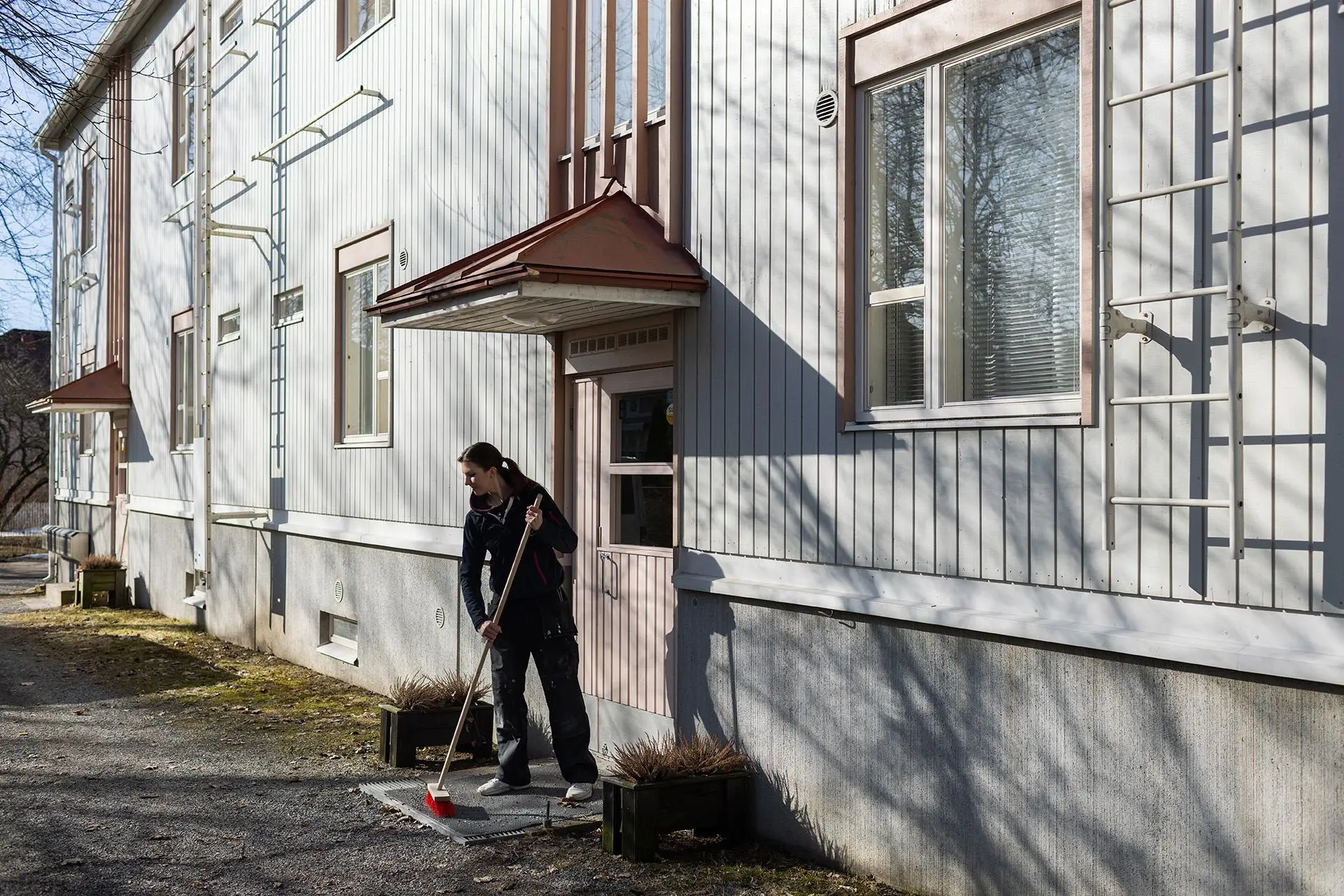 Jenniina Kuusrainen lakaisee kaksikerroksisen pienkerrostalon oven edustaa.