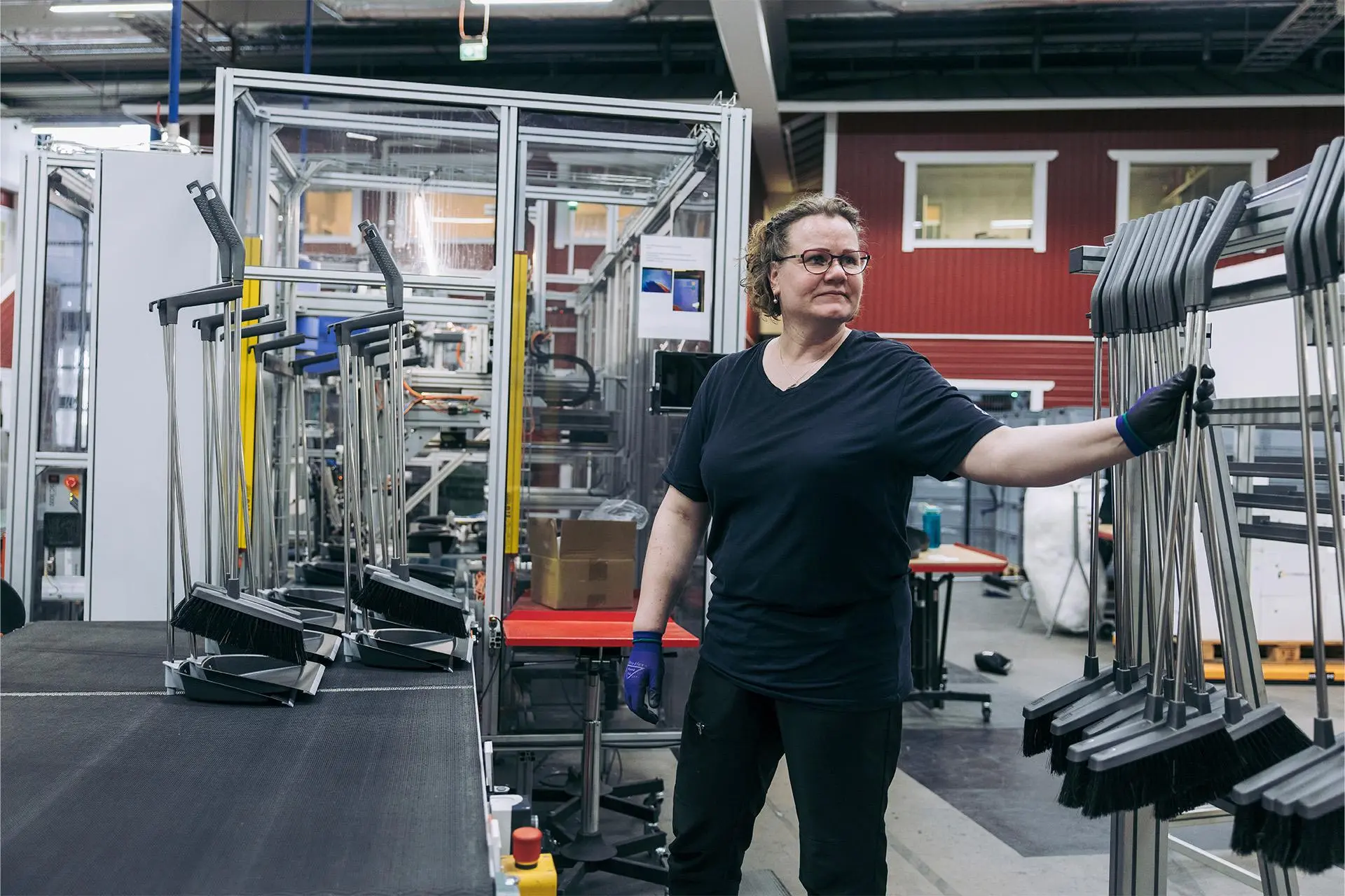 Heli Salminen vieressään teline, jossa on monia rikkaharjoja.