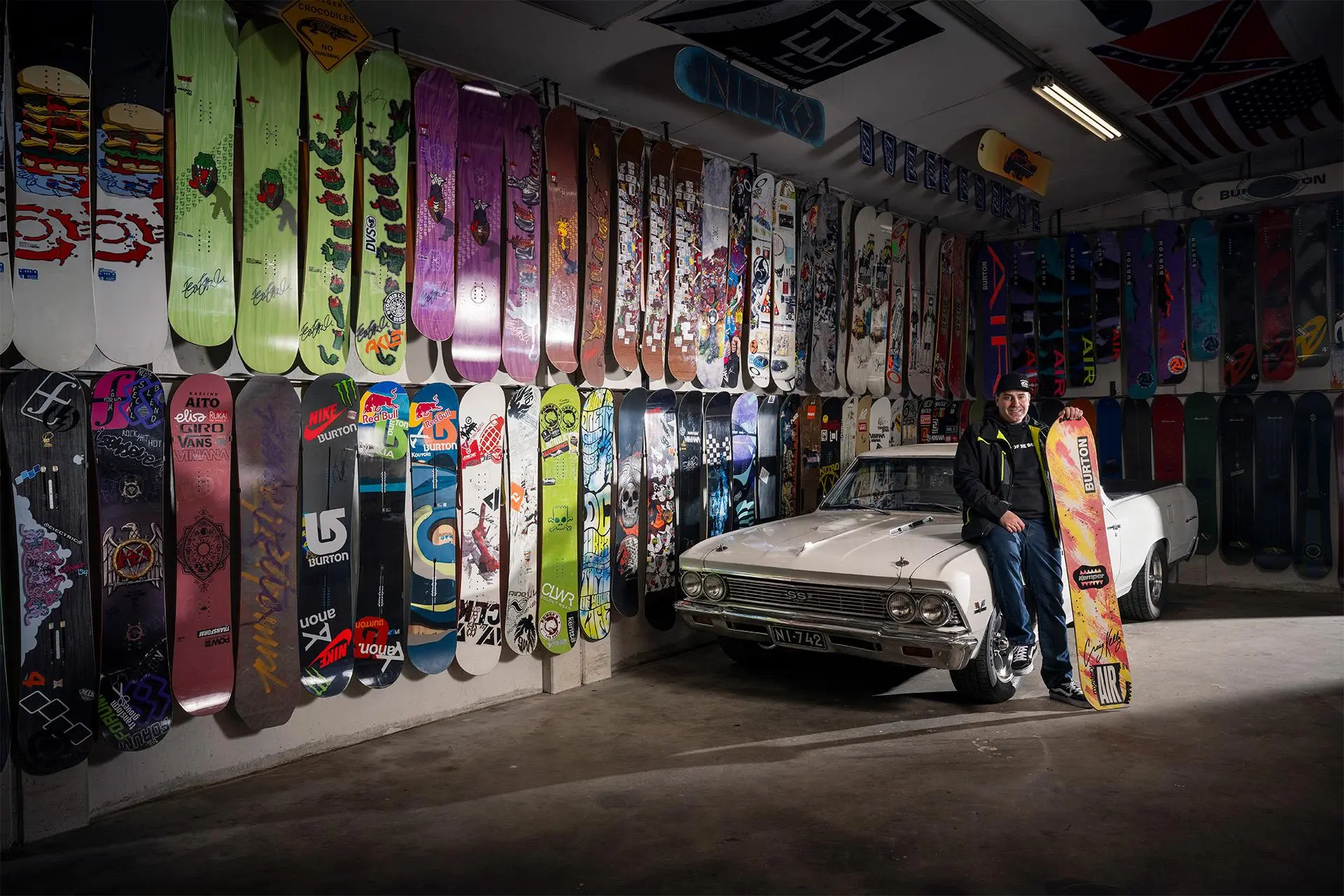 Mikko Halme nojailee autoon tallissa, jonka seinät on vuorattu lumilaudoilla.