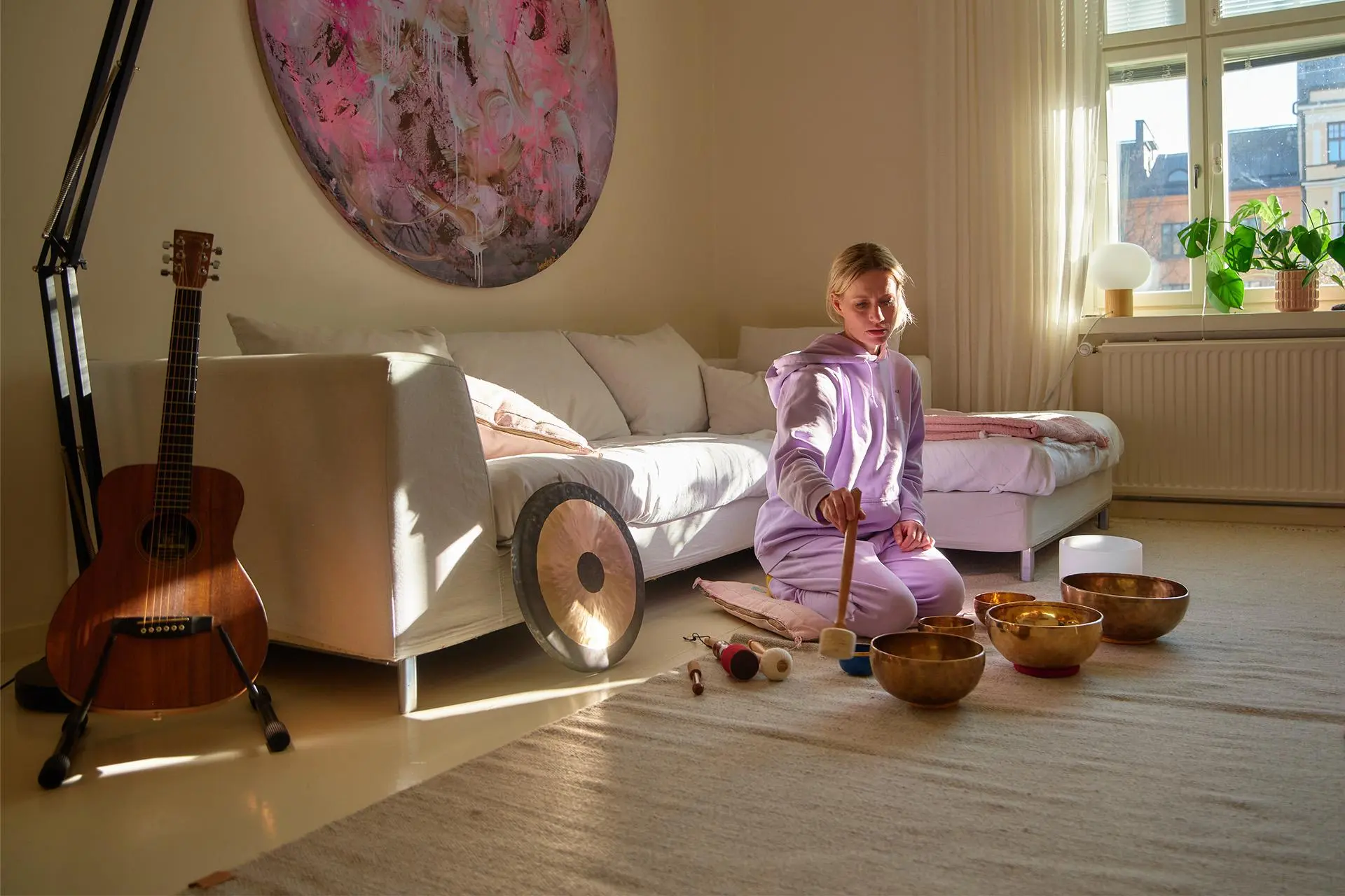 Minka Kuustonen soittaa äänimaljoja lattialla, taustalla valkoinen sohva ja pyöreä taideteos.