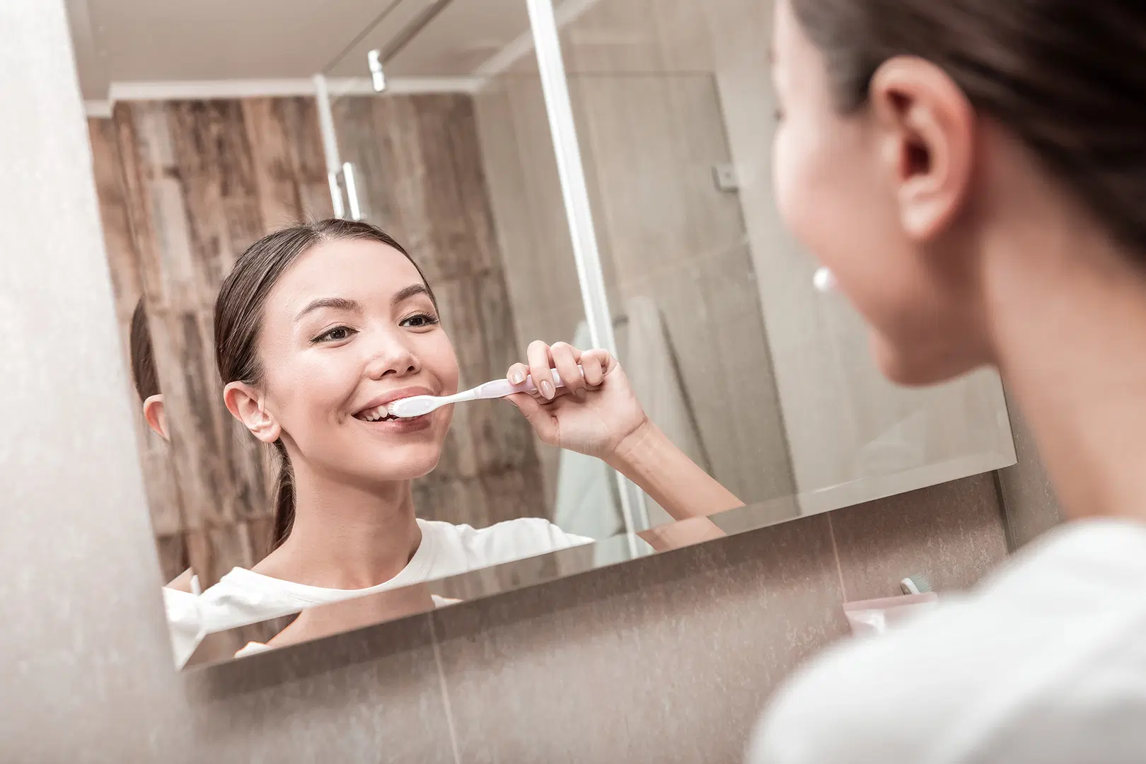 Nuori nainen harjaa hampaitaan peilin edessä.