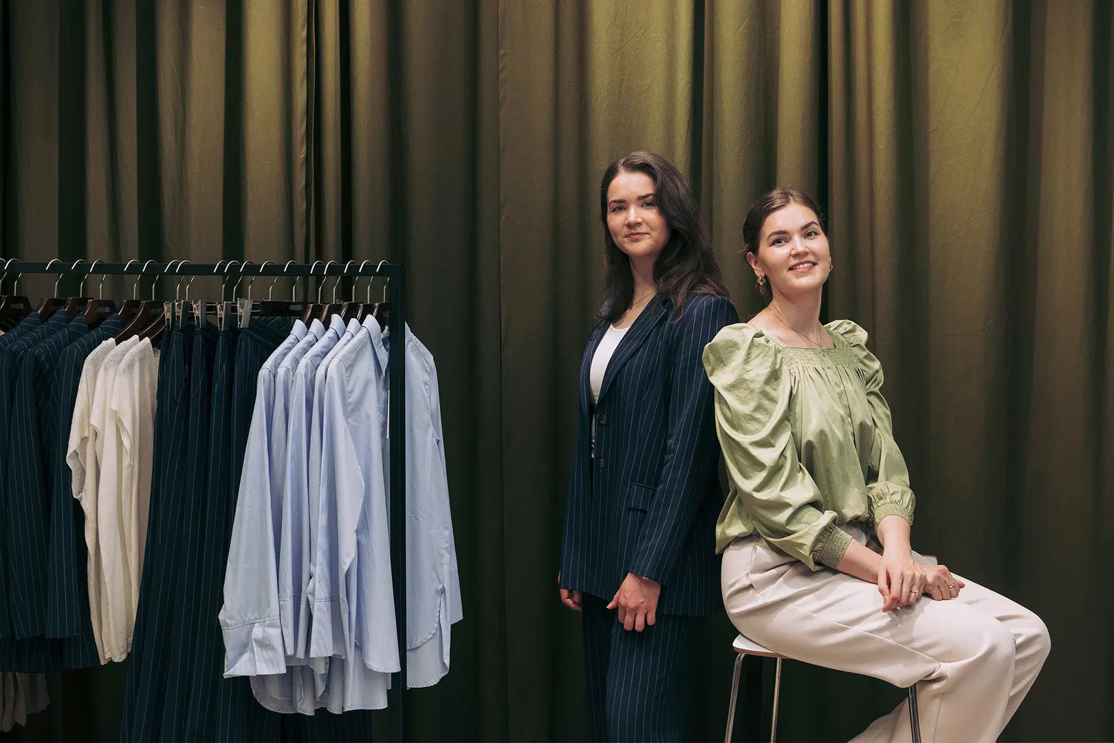Pauliina ja Katriina Virtanen sekä vaaterekki, jossa roikkuu kauluspaitoja ja siistejä housuja.
