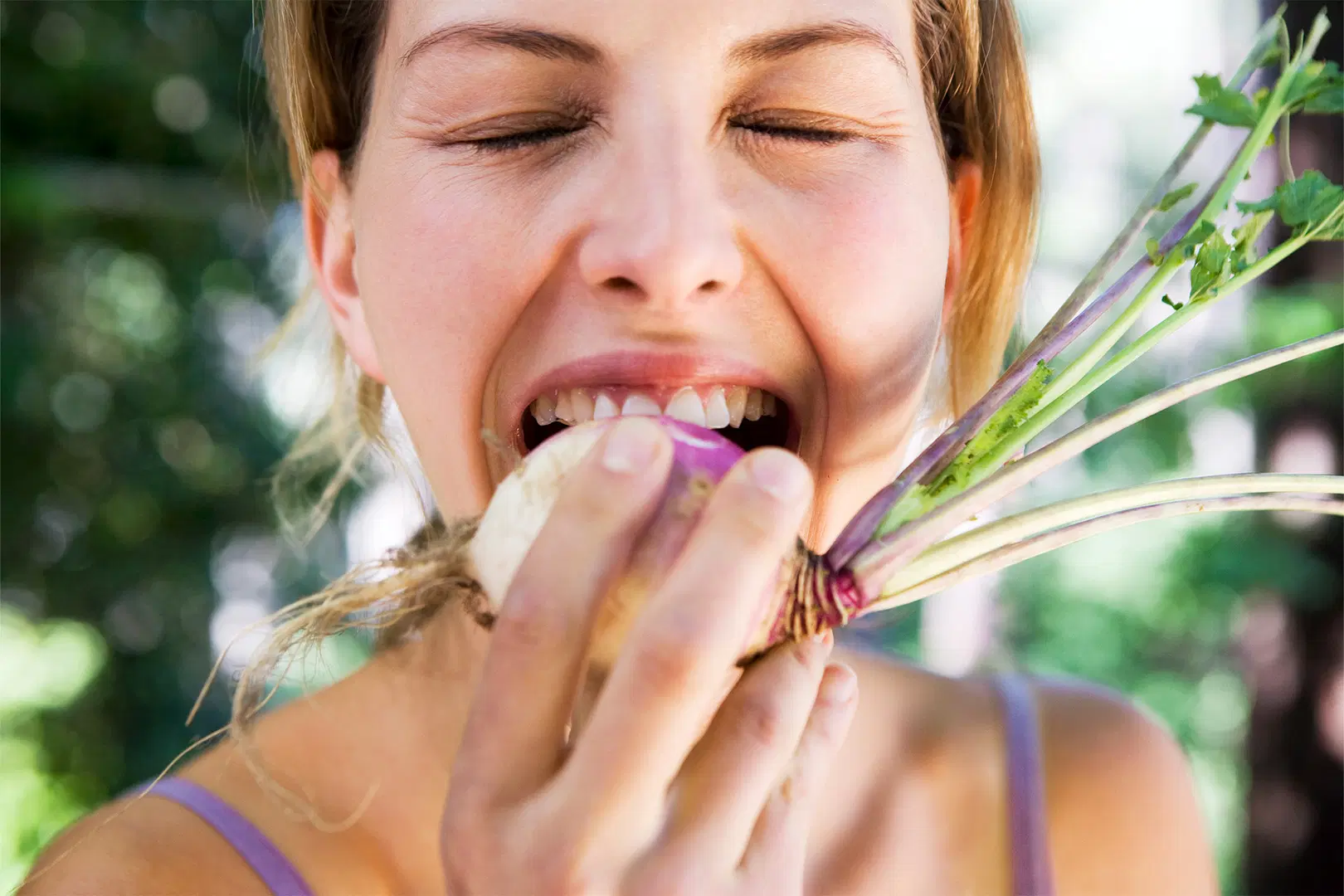 Henkilö haukkaa tuoretta naurista ulkona, silmät kiinni, vihreä tausta.