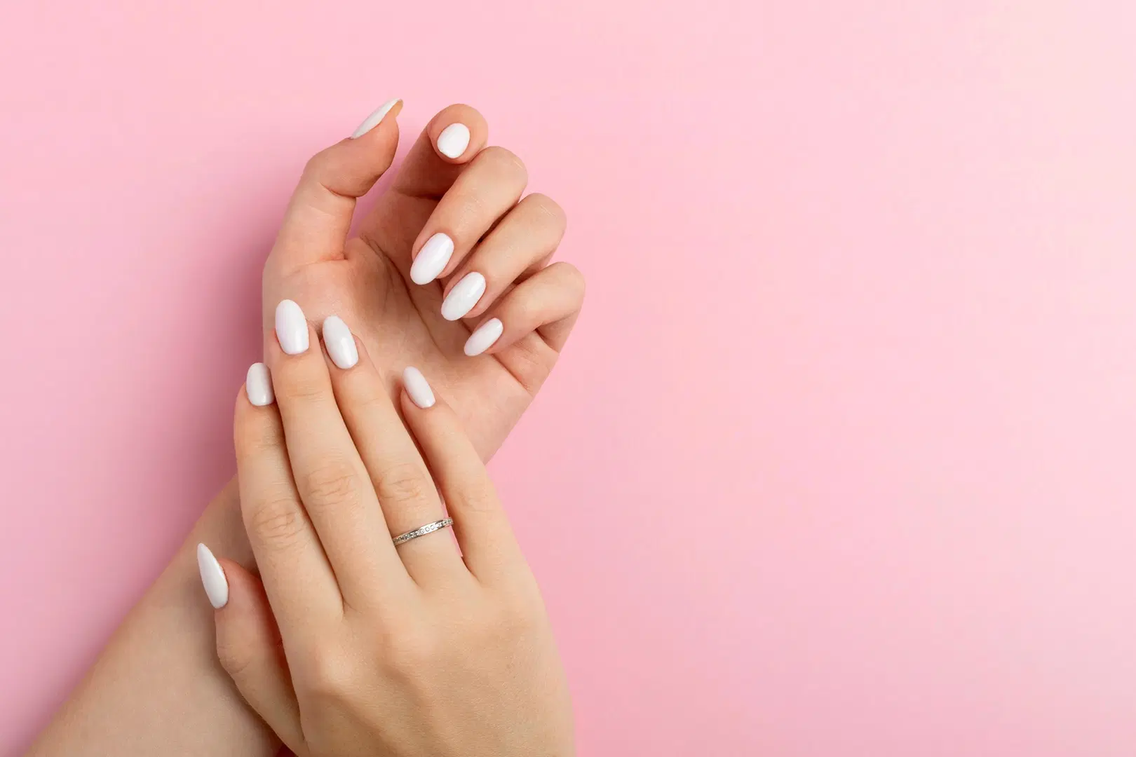 Naisen kädet vaaleanpunaista taustaa vasten, kynsissä vaalea lakkaus