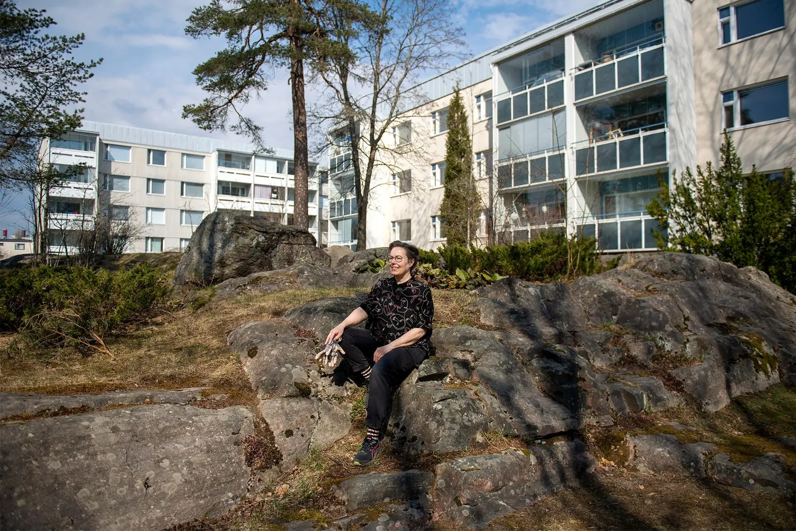 Kitti Suoranta istuu kalliolla kerrostalon edessä.