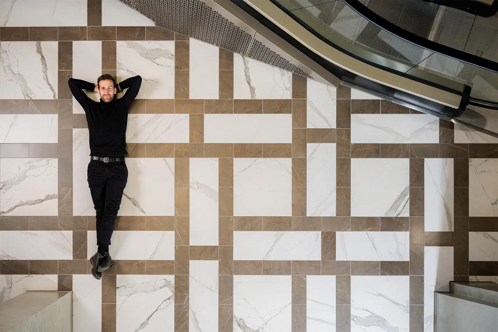 Mies makaa ruudukon päällä käden pään takana.