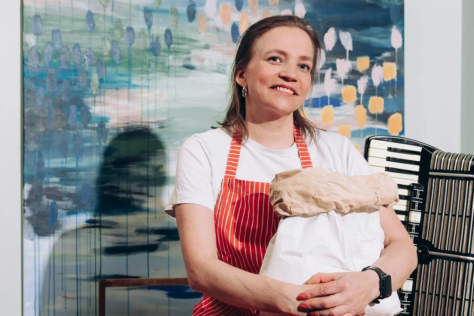 Tietokirjailija Mari Koistinen kädessään jauhopussi, taustalla värikäs maalaus