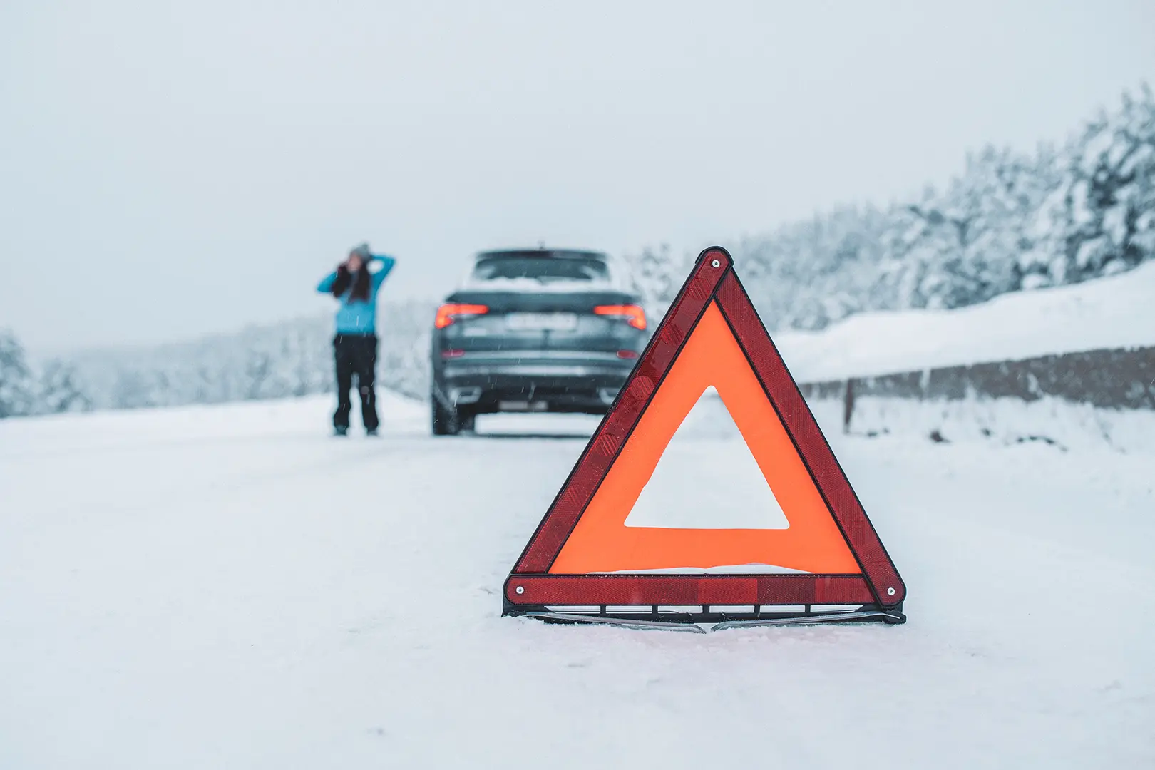 Varoituskolmio, jonka takaa näkyy auto ja sen vieressä kuljettaja puhelimessa.