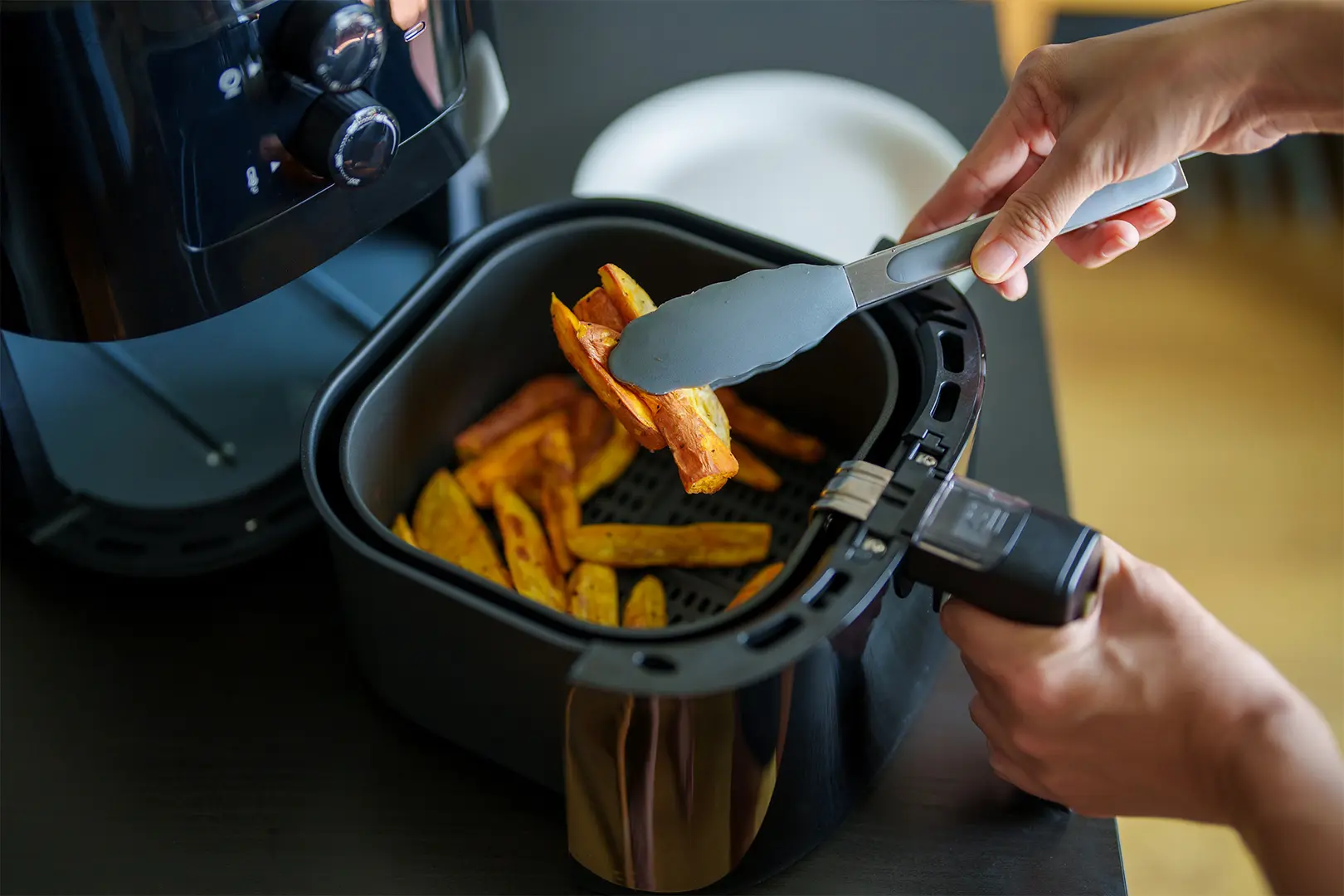 Airfryer täynnä ranskalaisia ja kädet, joissa on lasta, jolla sekoitetaan ranskalaisia.