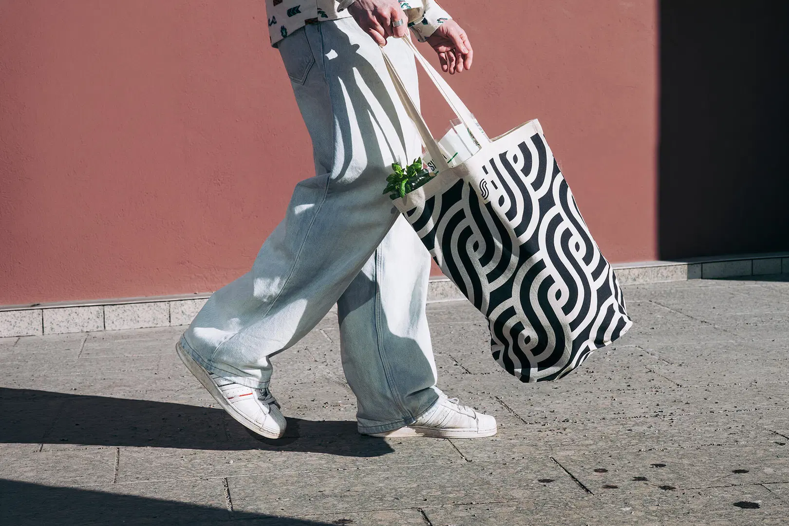 Nuori mies kävelee kesäisellä kadulla S-ryhmän kangaskassi kädessään.