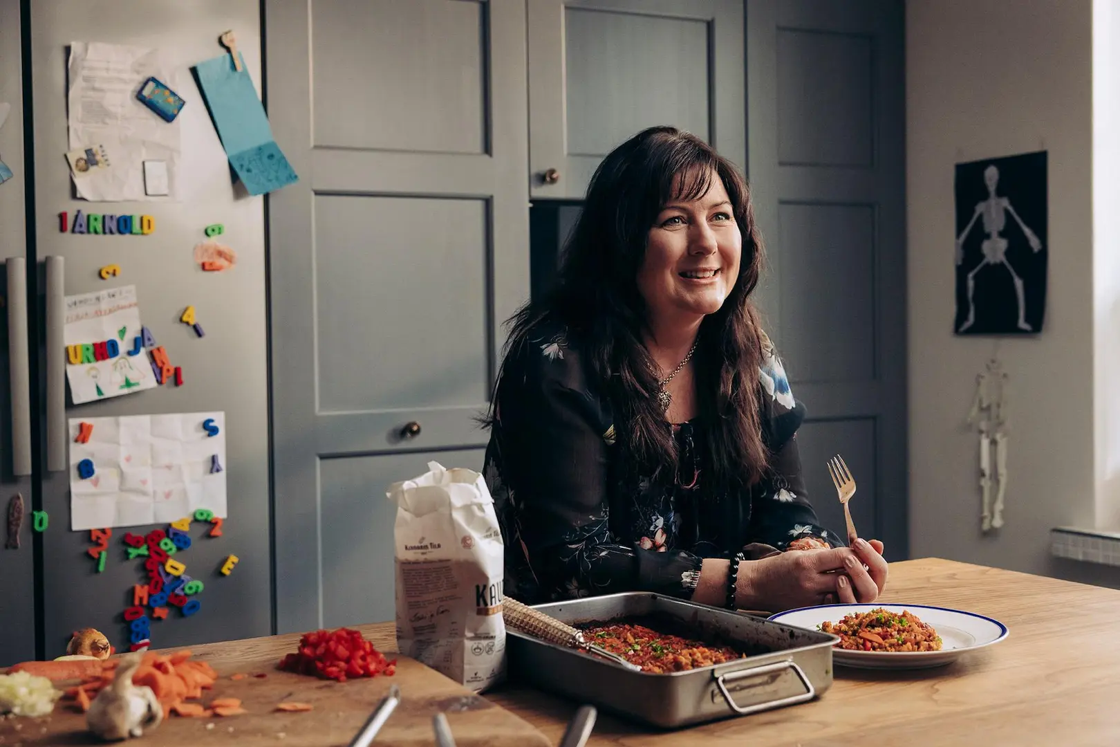 Terhi Kinnari nojaa keittiön tasoon, jossa on uunivuoassa ruokaa.