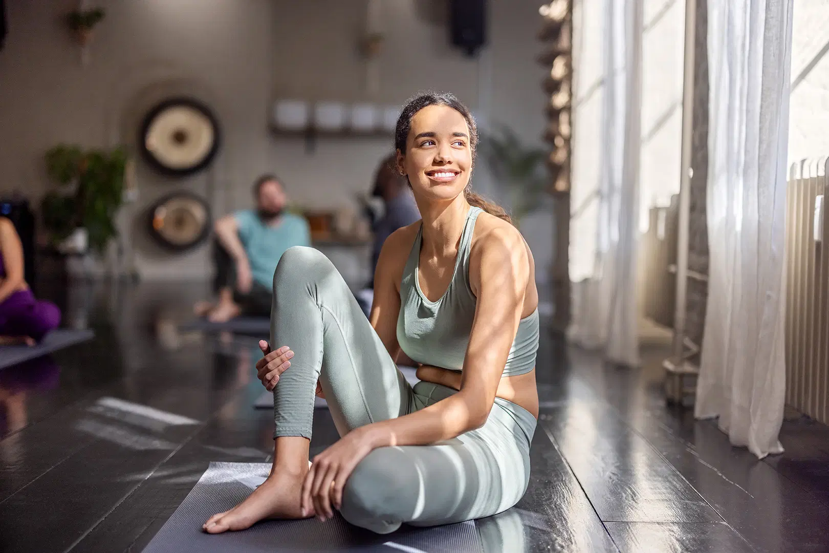 Nainen istuu ikkunan edessä päällään urheilullinen paita ja housu.