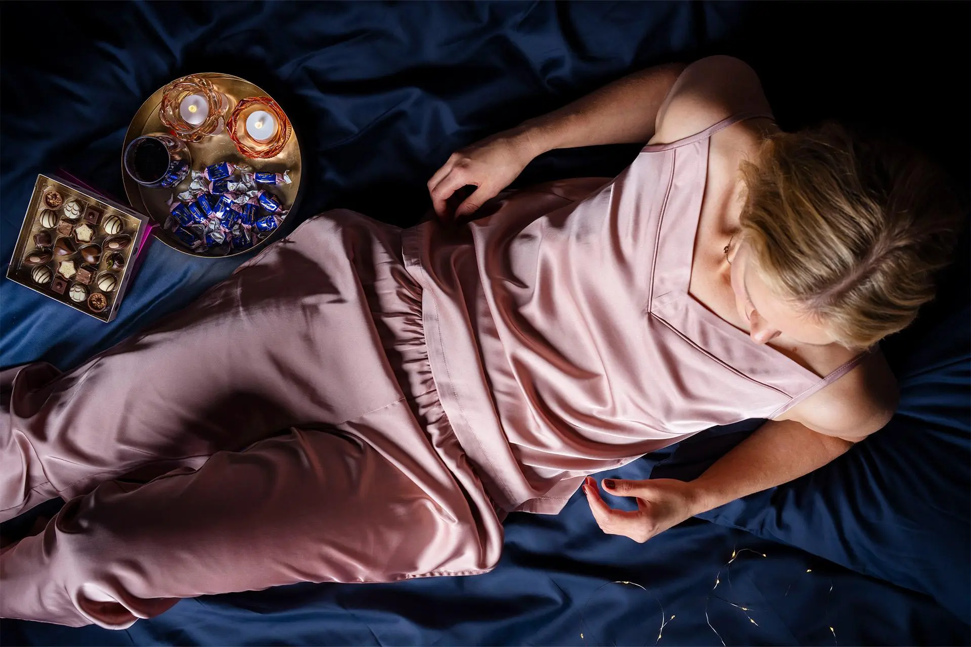 Mallilla päällään satiiniset pyjamahousut ja -toppi, lautasella kynttilöitä ja suklaata