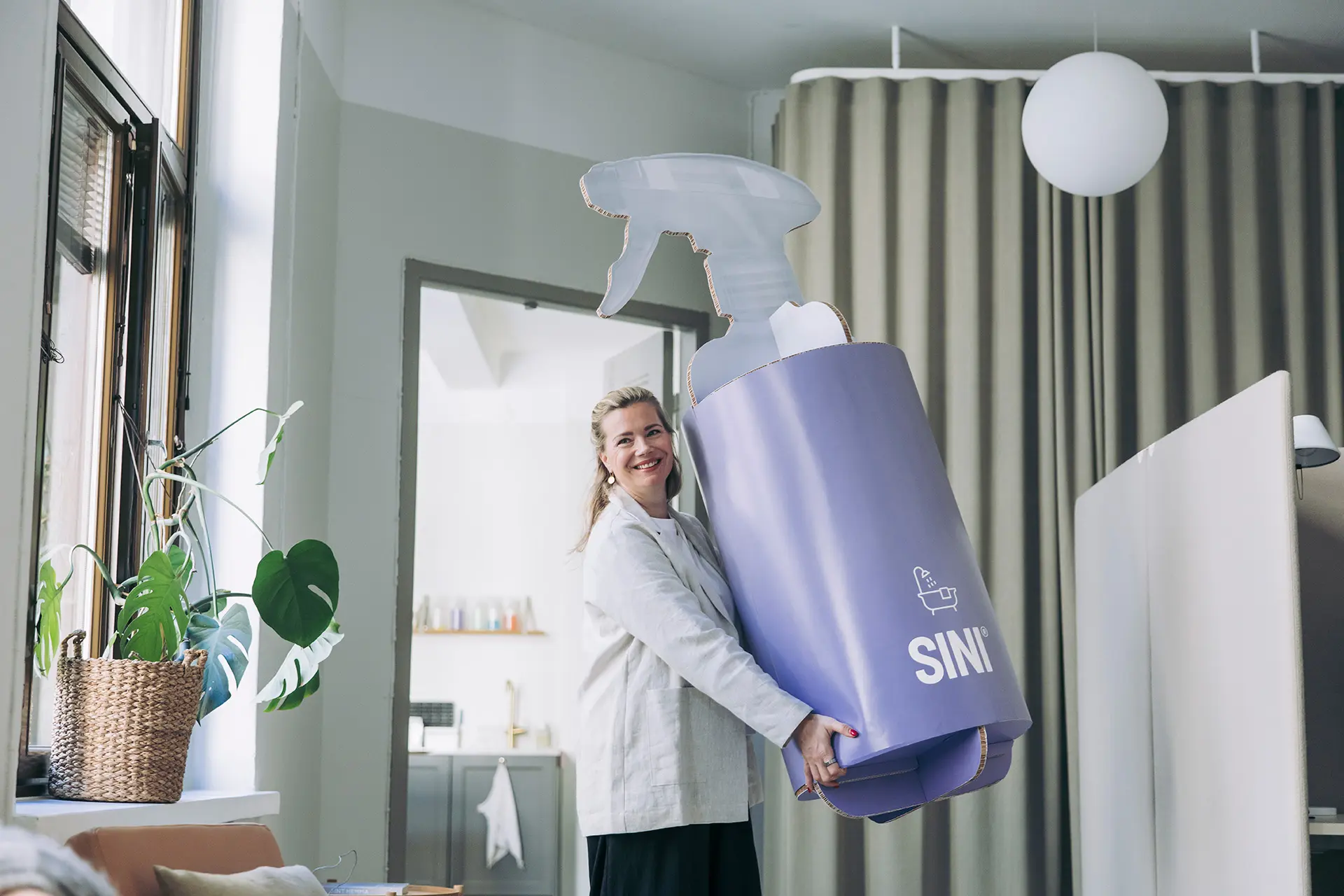 Johanna Hamro-Drotz kantaa valtavaa, pahvista Sini-suihkepulloa.