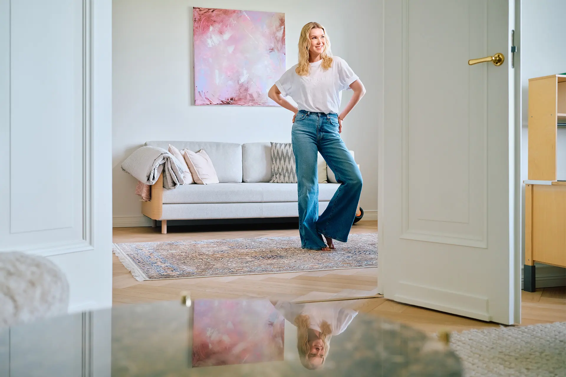 Tuija Pehkonen seisoo huoneessa, jossa on sohva ja suuri, abstrakti maalaus