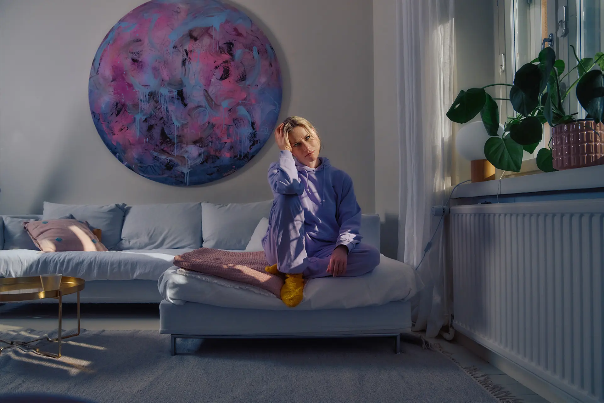 Minka Kuustonen istuu kotona vaaleansinisellä sohvalla, takana pyöreä taideteos