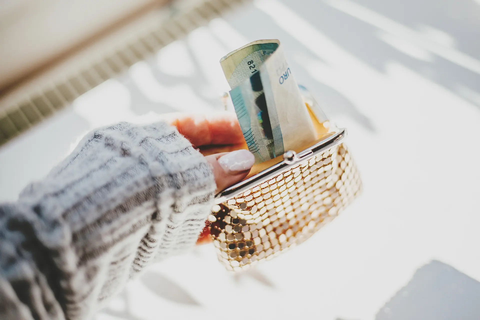 Nainen pitelee avointa kukkaroa, josta törröttää seteli