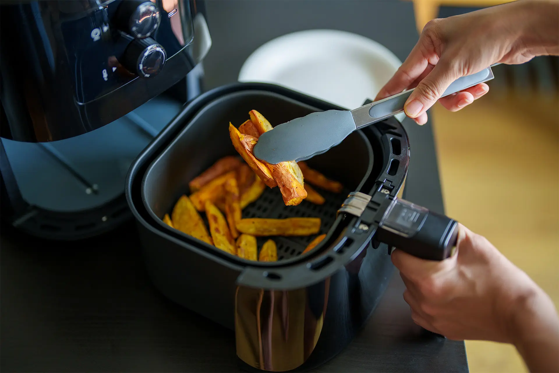 Airfryer täynnä ranskalaisia ja kädet, joissa on lasta, jolla sekoitetaan ranskalaisia.