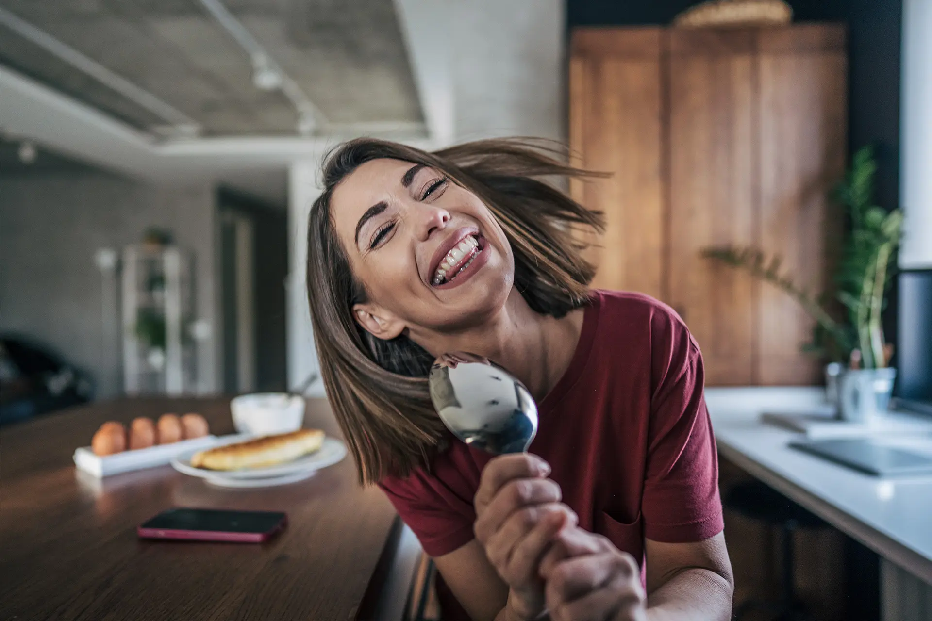 Nainen keittiössä hiukset hulmuten, kädessä lusikka kuin mikrofoni