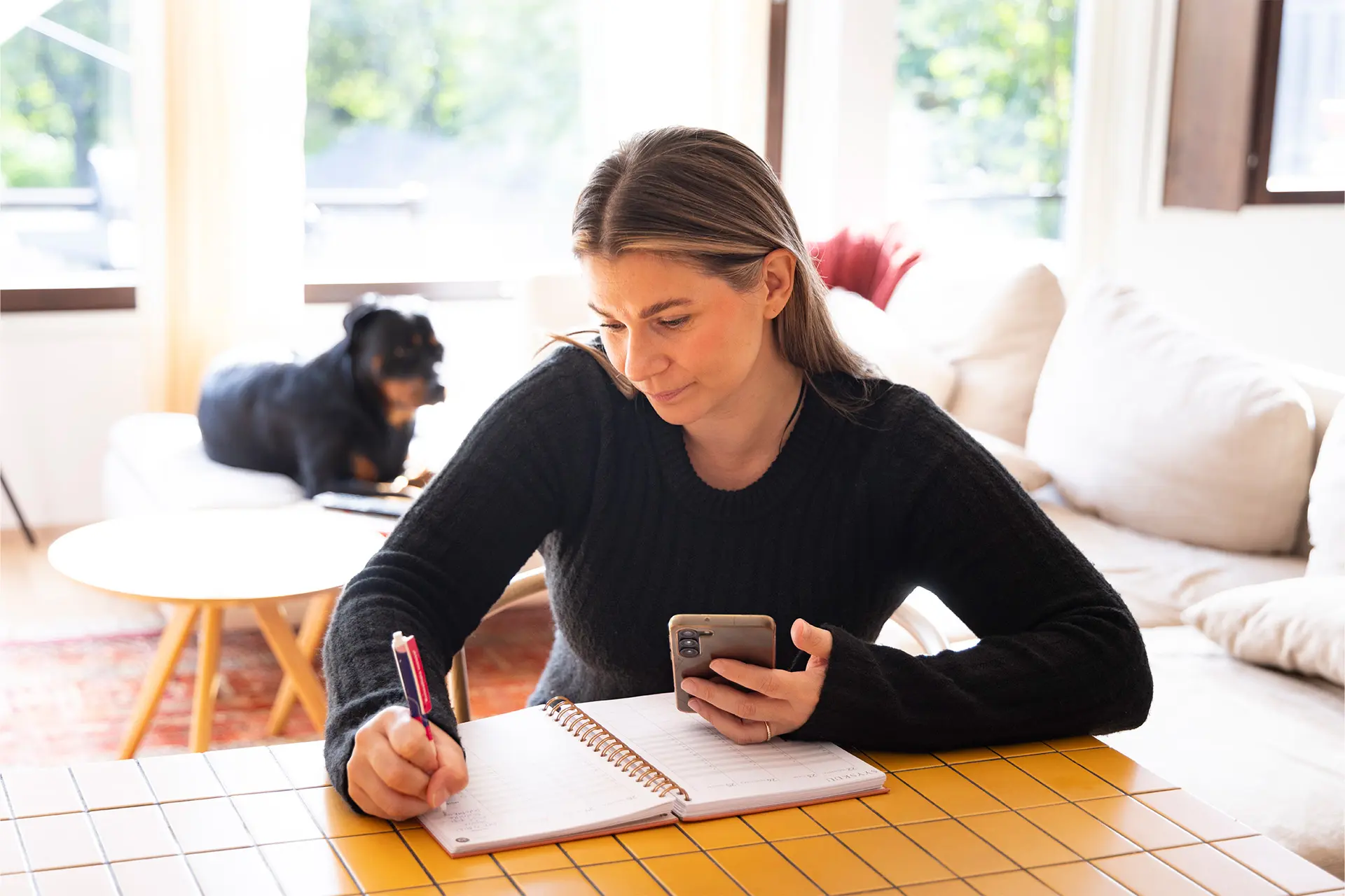Saana Opacic kirjoittaa kynällä vihkoon, kädessä puhelin, taustalla musta koira.