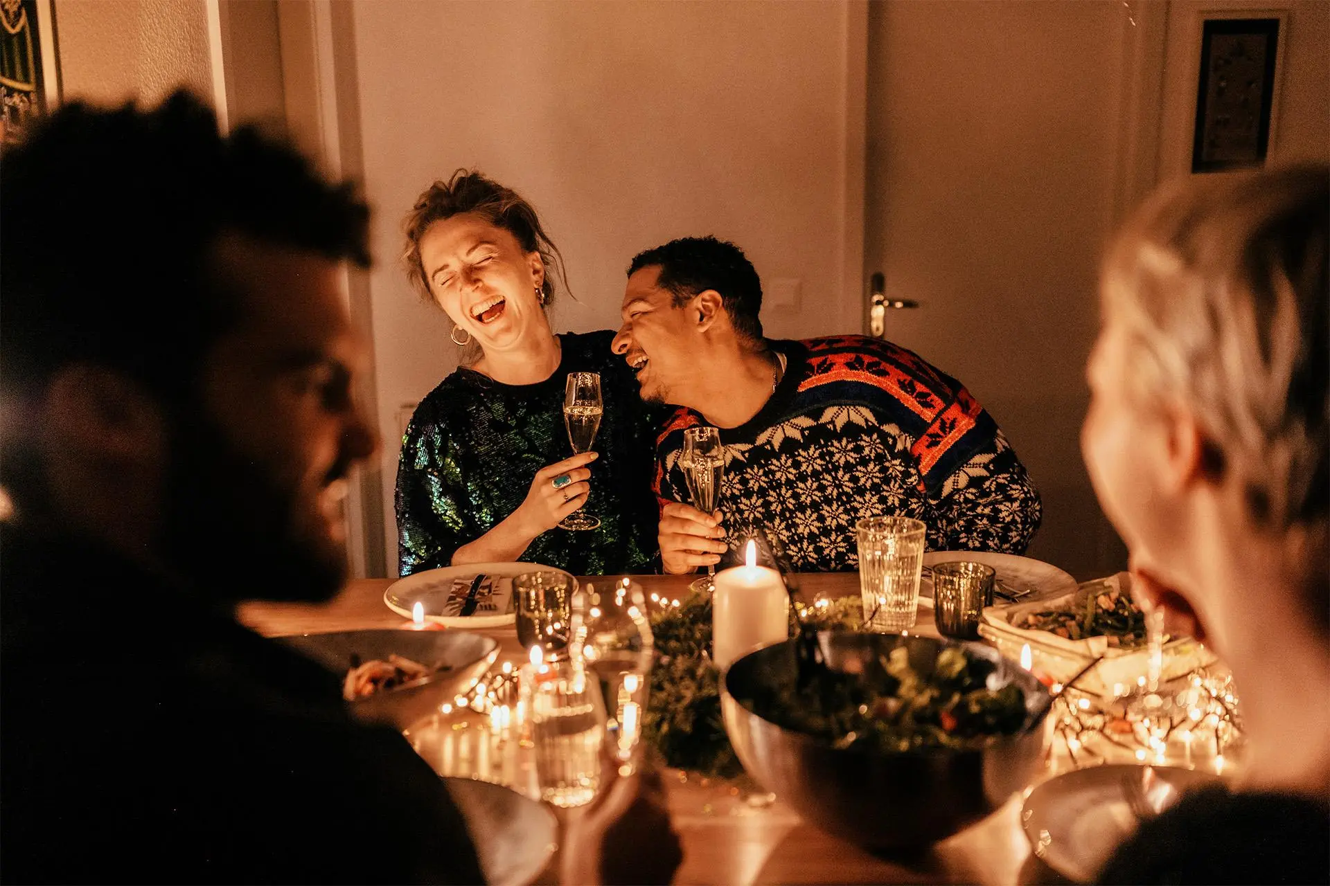 Nainen ja mies nauravat pöydän ääressä kuohuviinilasit kädessä.