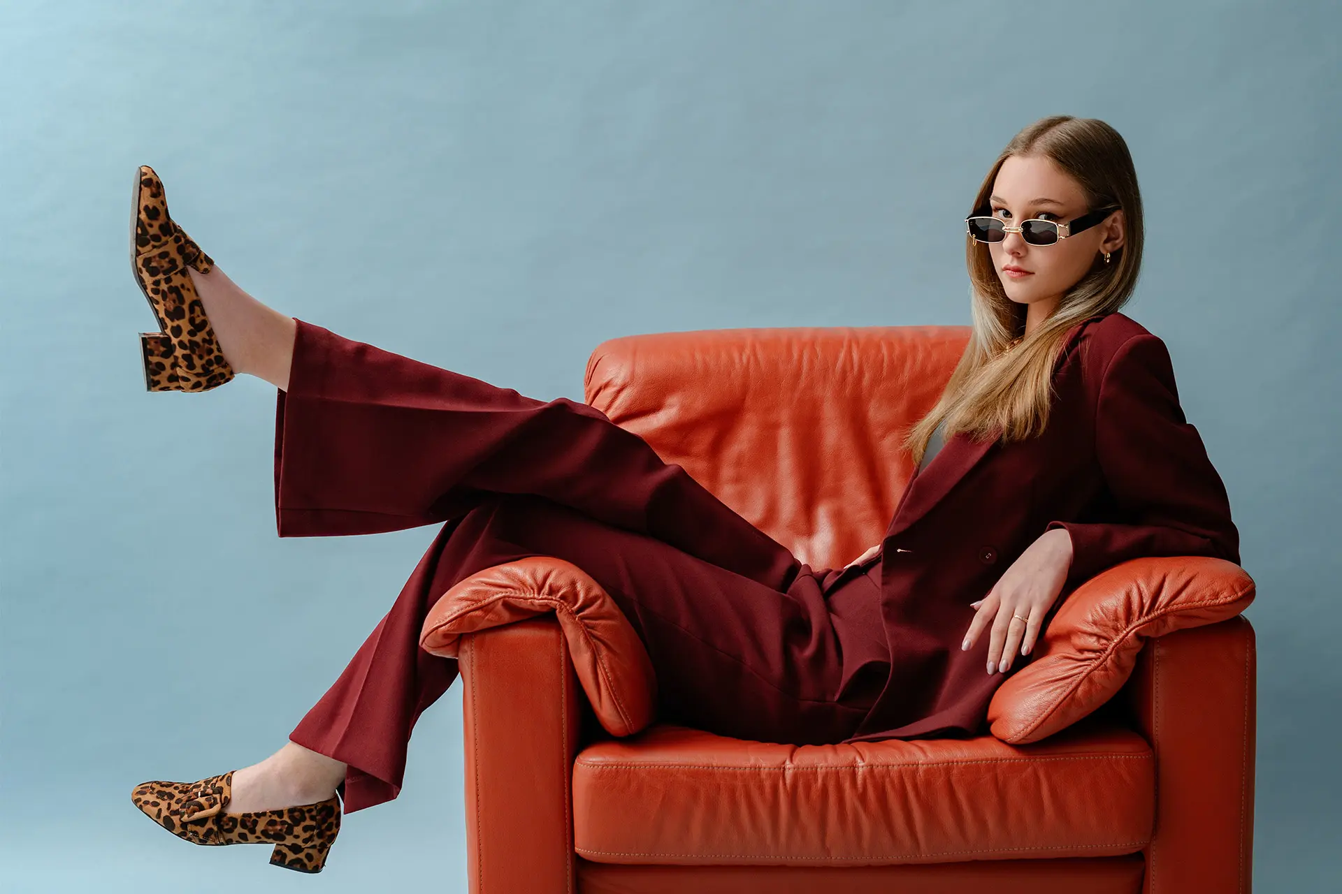 Viininpunaiseen asuun pukeutunut nainen poseeraa oranssissa nojatuolissa