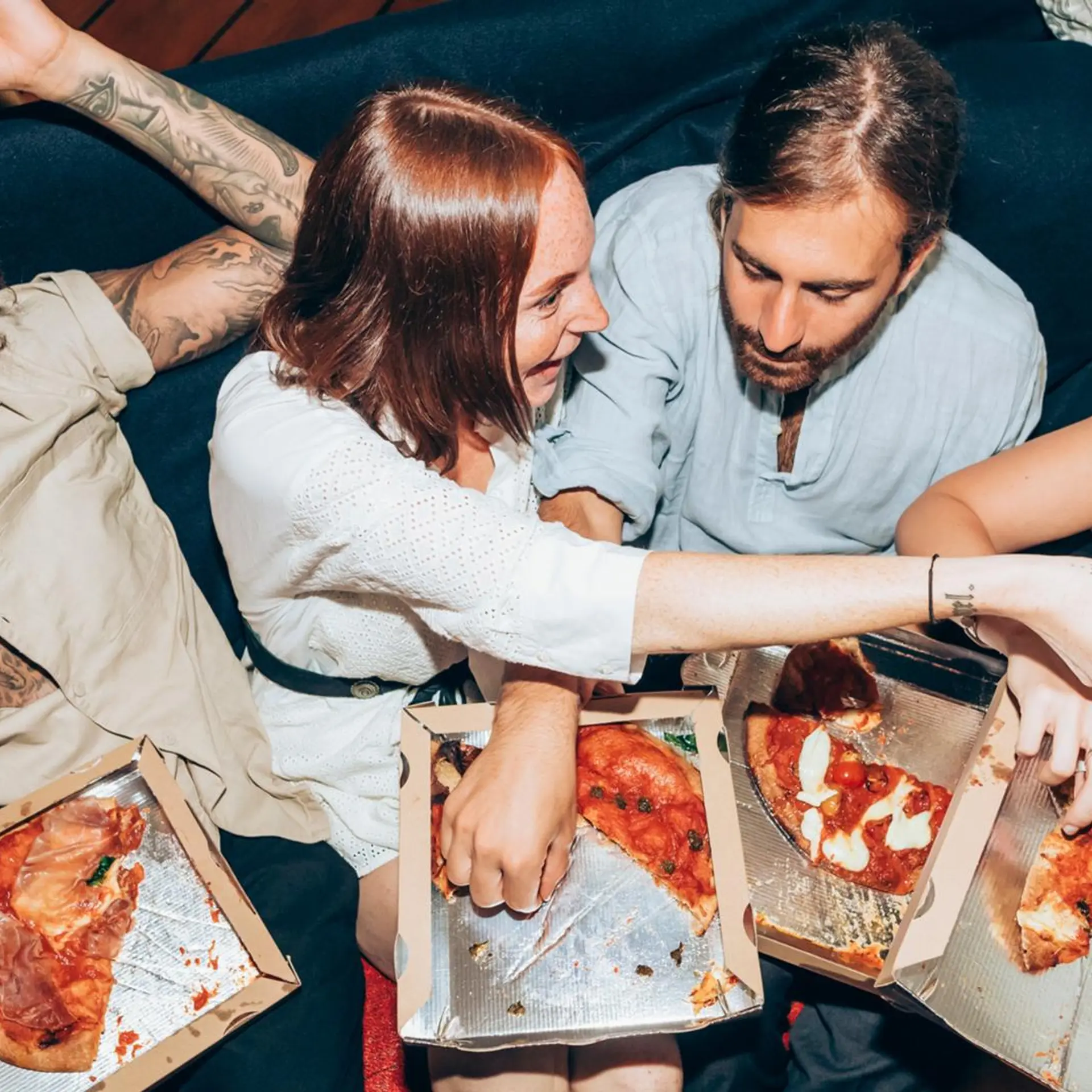 Kolme naista ja yksi mies syövät laatikoista pizzaa.