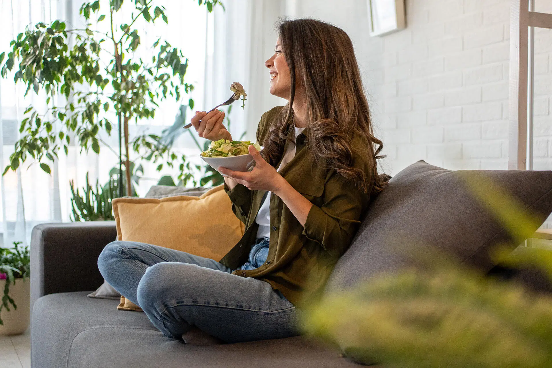 Nainen istuu risti-istunnassa sohvalla ja syö salaattia kulhosta.
