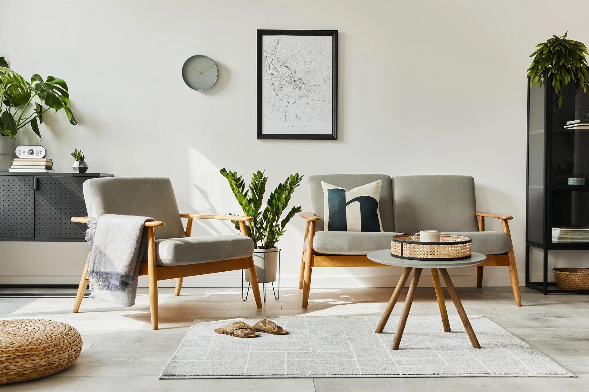 Vaalea moderni olohuone: harmaat nojatuolit, pyöreä sohvapöytä, vaalea matto, viherkasveja ja seinätaulu.