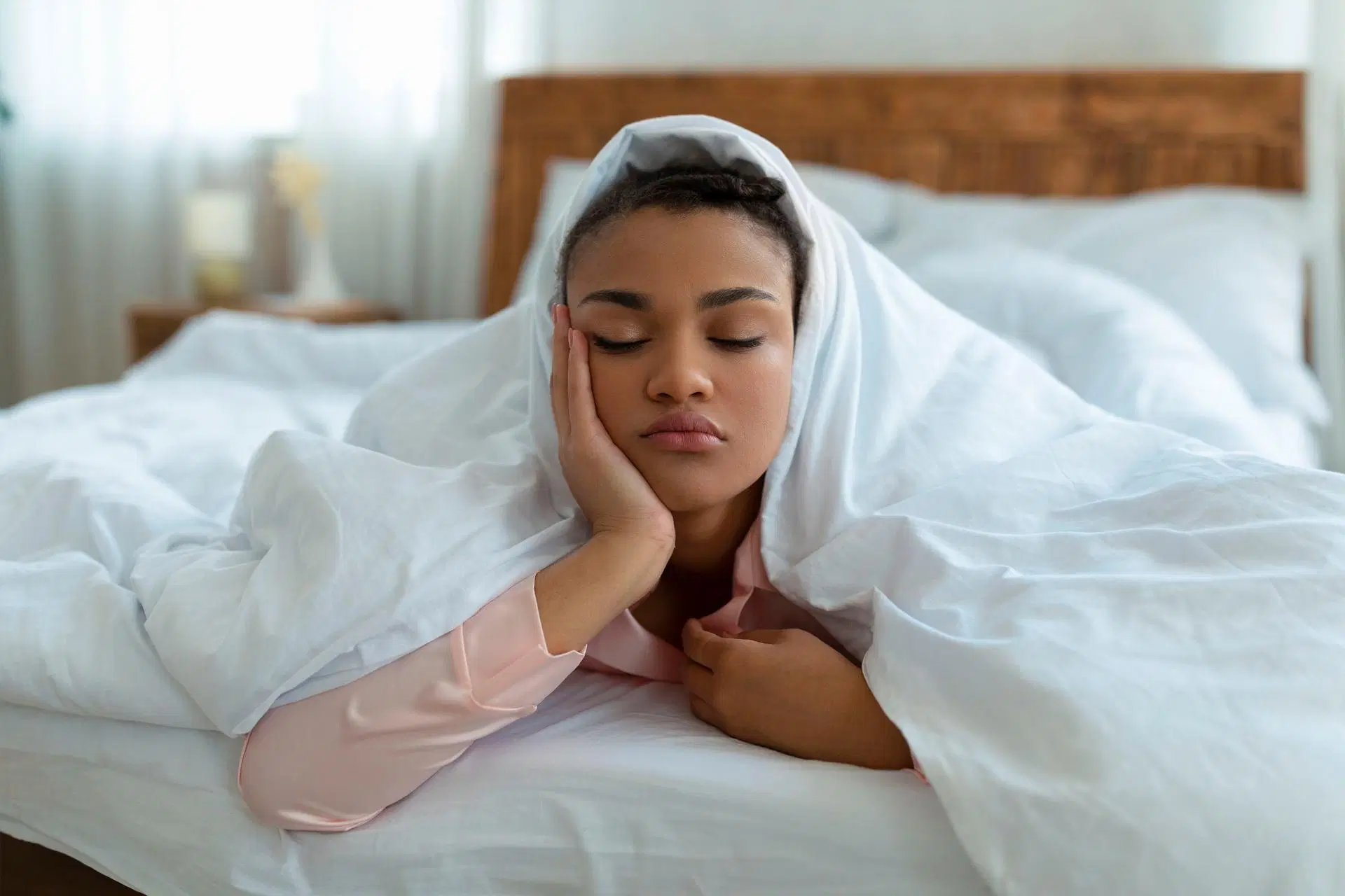 Nainen makaa väsyneenä peiton alla käsi poskella