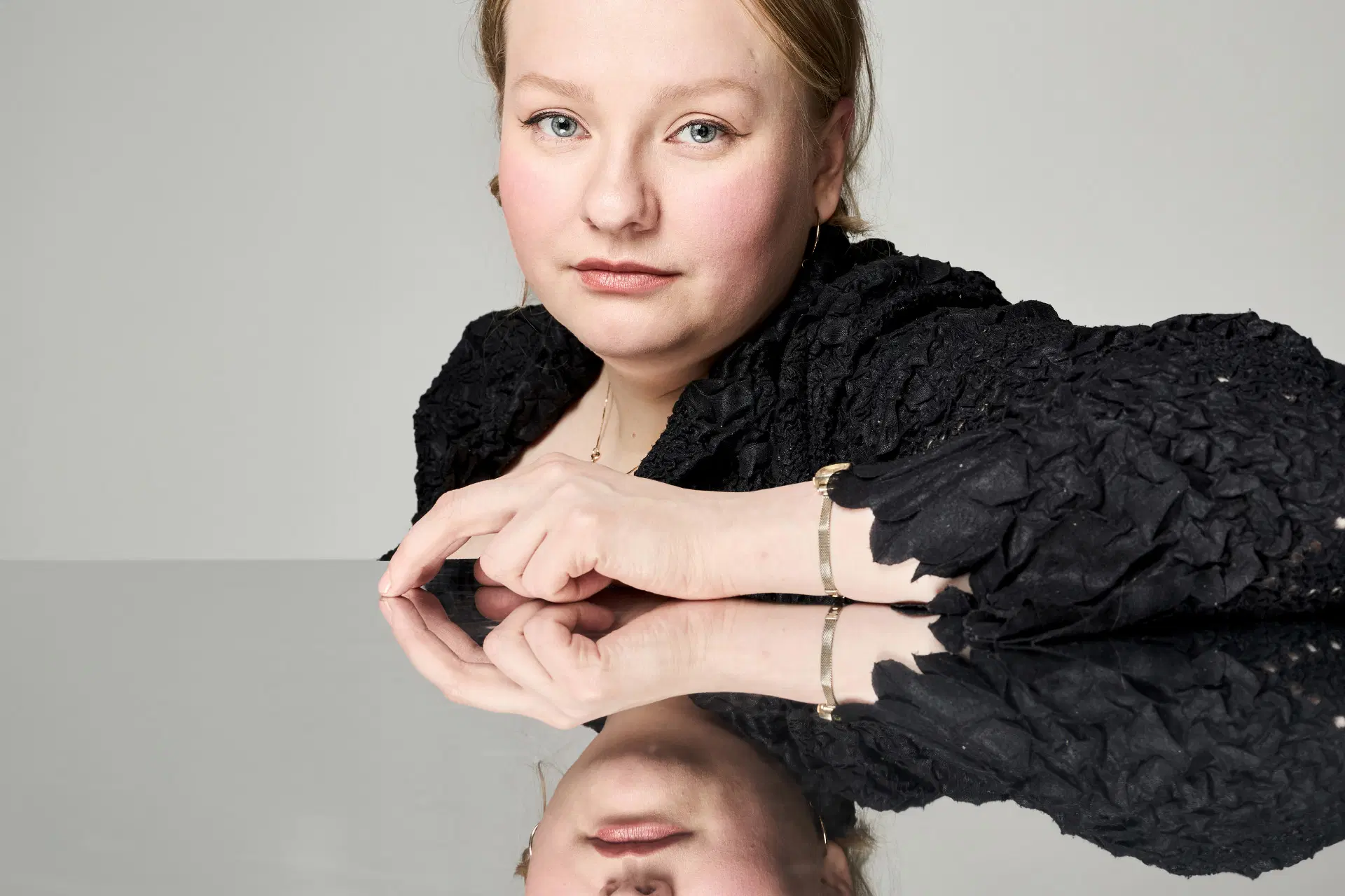 Mielinauhan suunnittelija Enni Lähderinne istuu ja nojaa pöytätasoon, jonka peilipinnasta hän heijastuu.