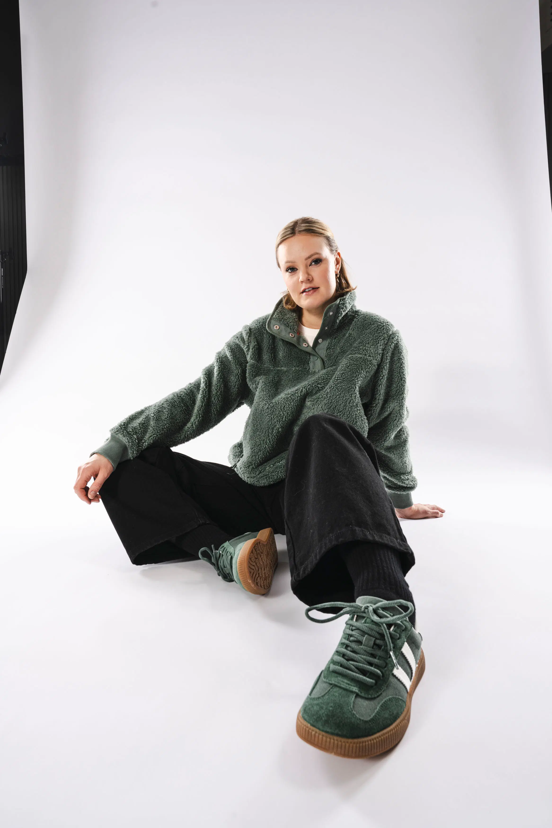 Mallilla päällä vihreä fleecepaita, mustat farkut ja vihreät tennarit.