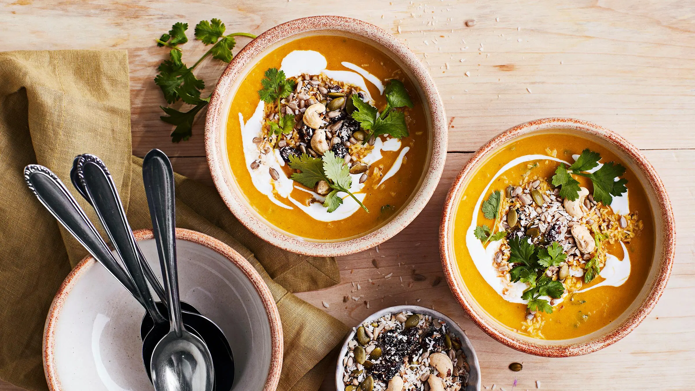 Kaksi lautasellista porkkana-kookoskeittoa. Annosten päällä siemensekoitusta ja korianteria.