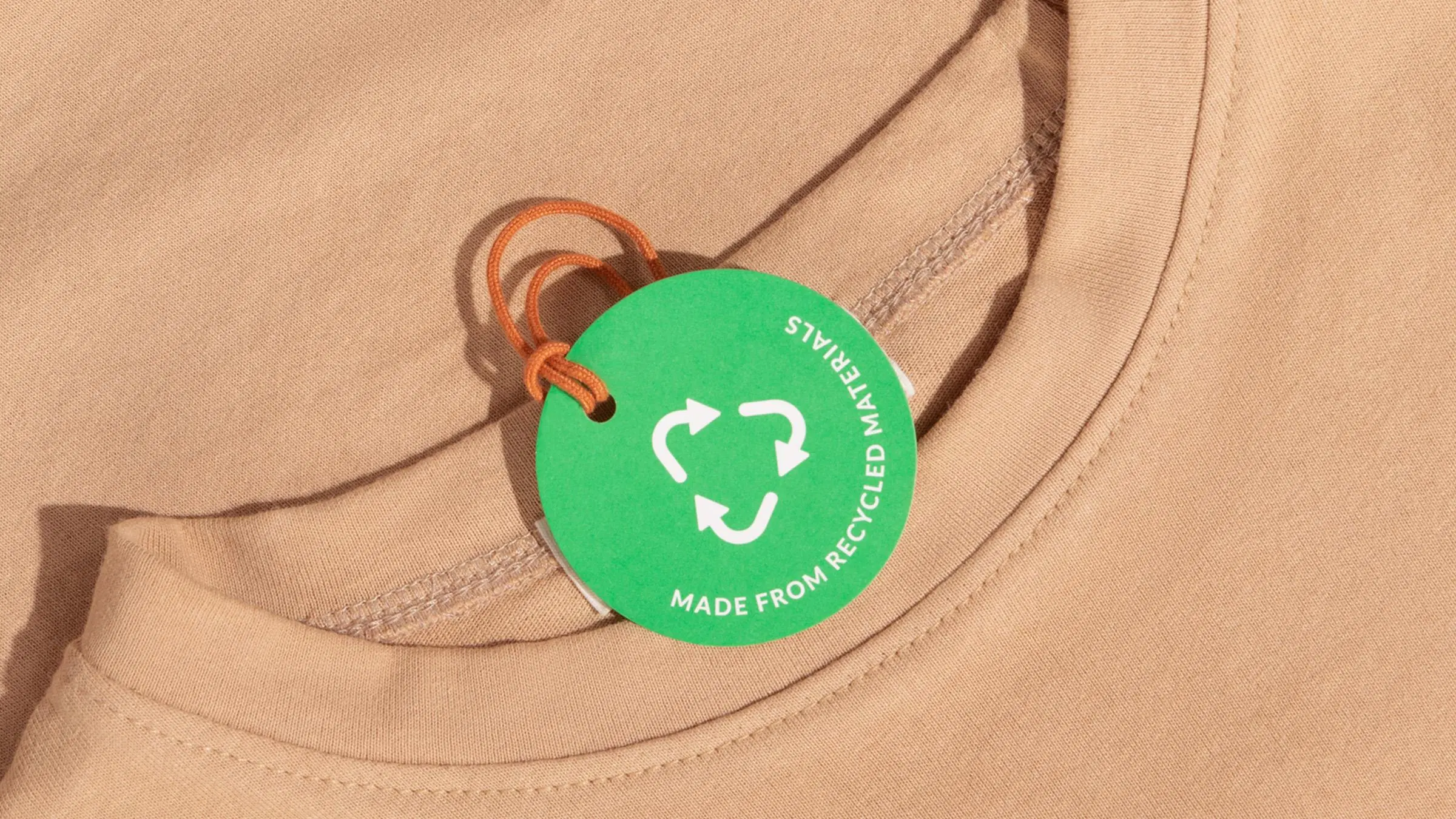 Beigen t-paidan kaulus, jossa on kiinni vihreä kierrätysmerkki