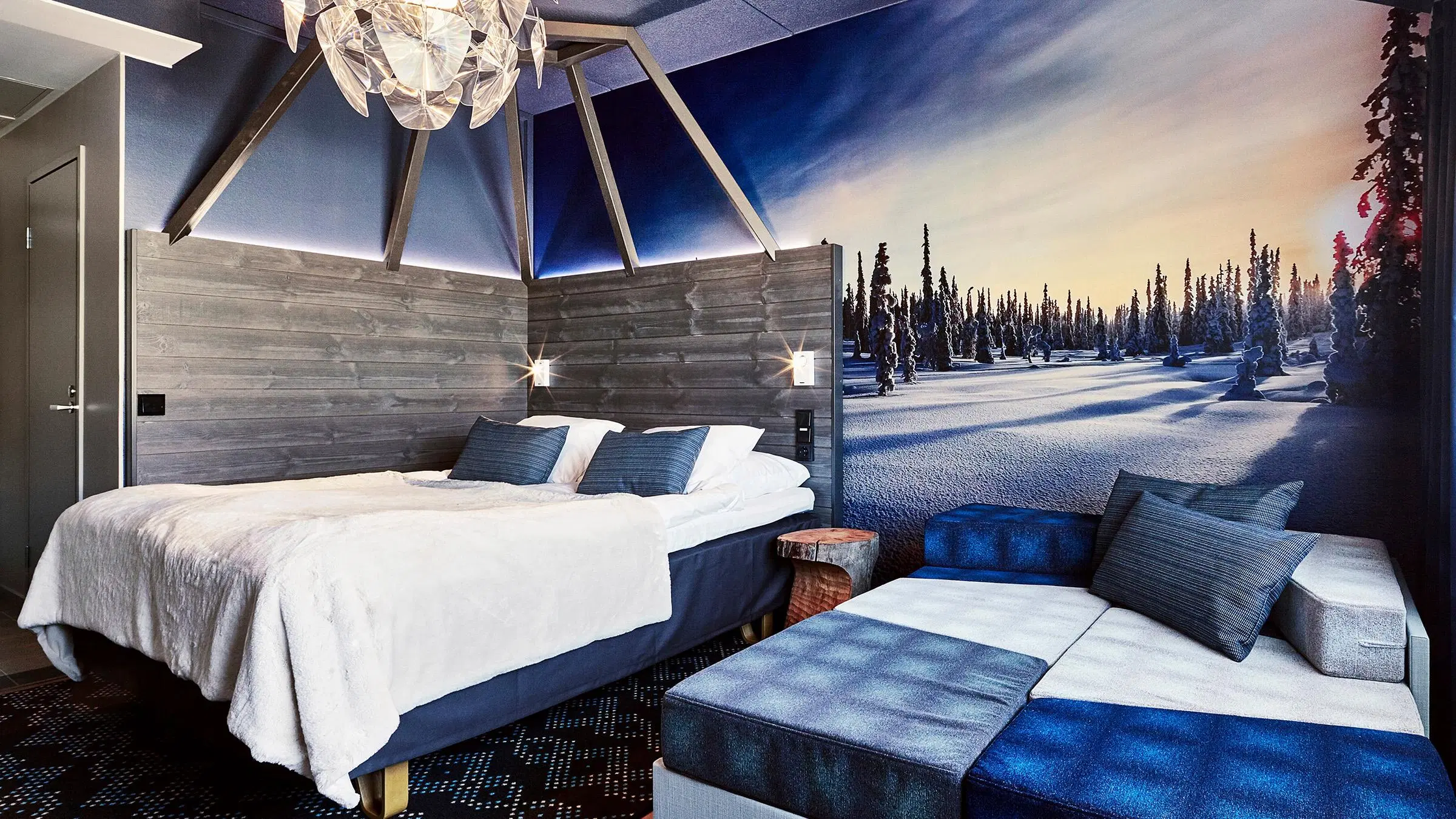 Hotellihuone, jossa tapettina valokuva lumisesta metsästä