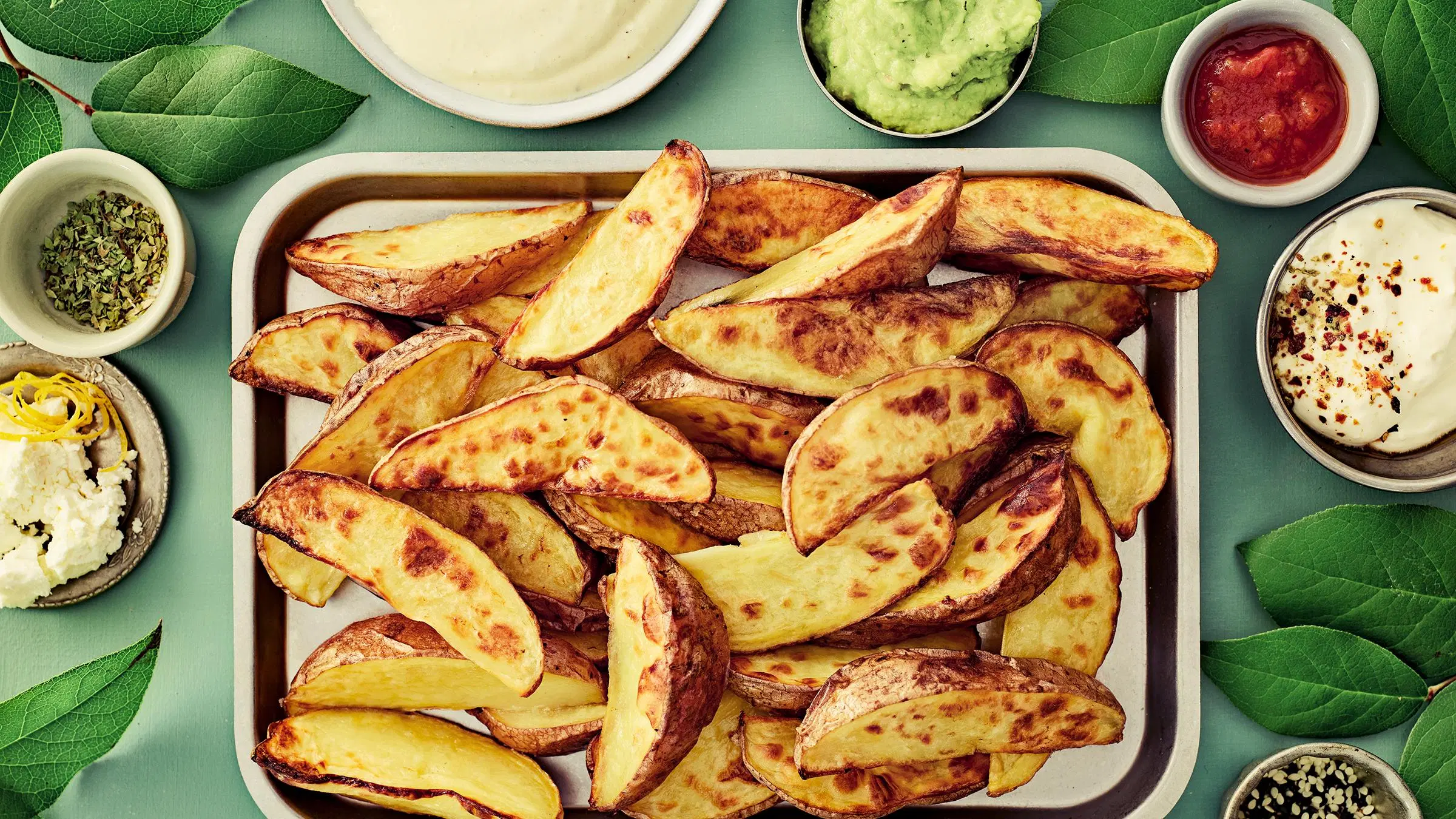 Rapeita lohkoperunoita vadilla ja eri makuisia dippejä pienissä kulhoissa.