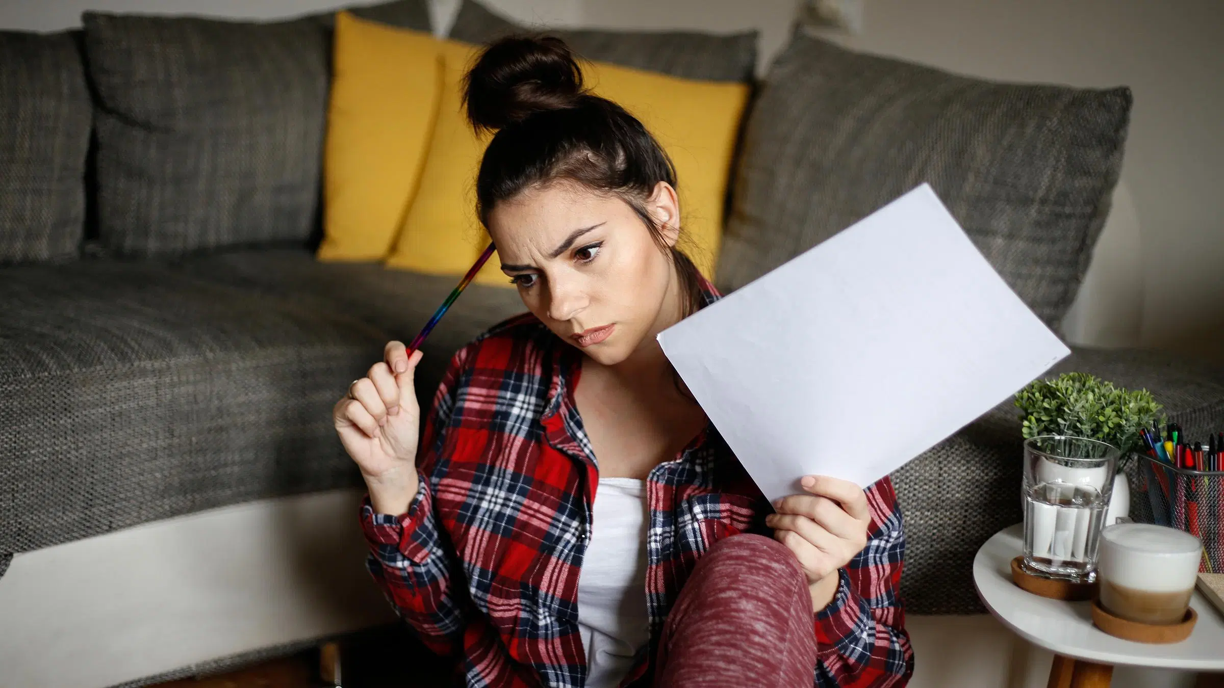 Naisella on kädessä paperia ja kynä, näyttää pohtivalta.