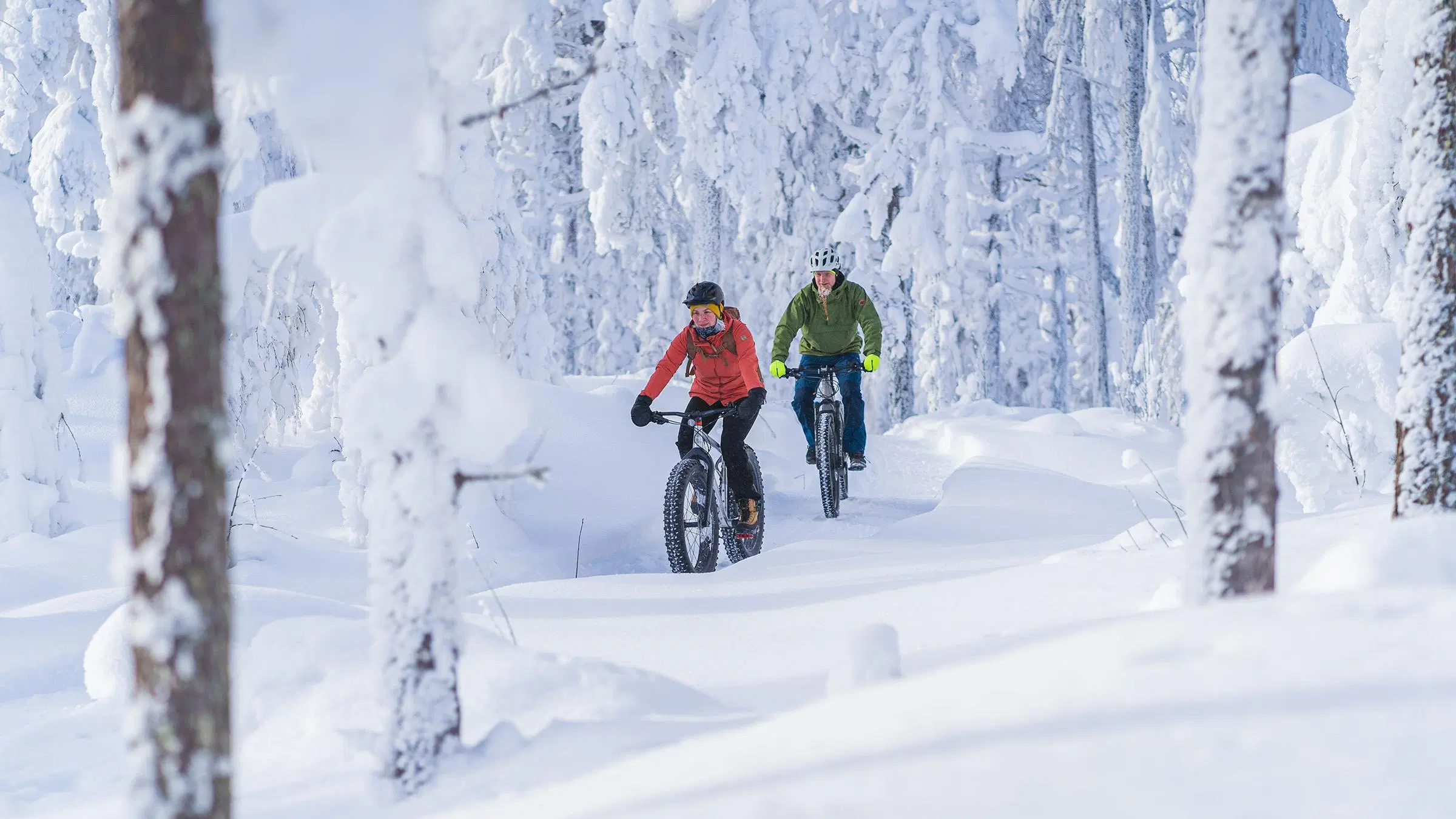 Kaksi talvipyöräilijää lumisessa metsässä.