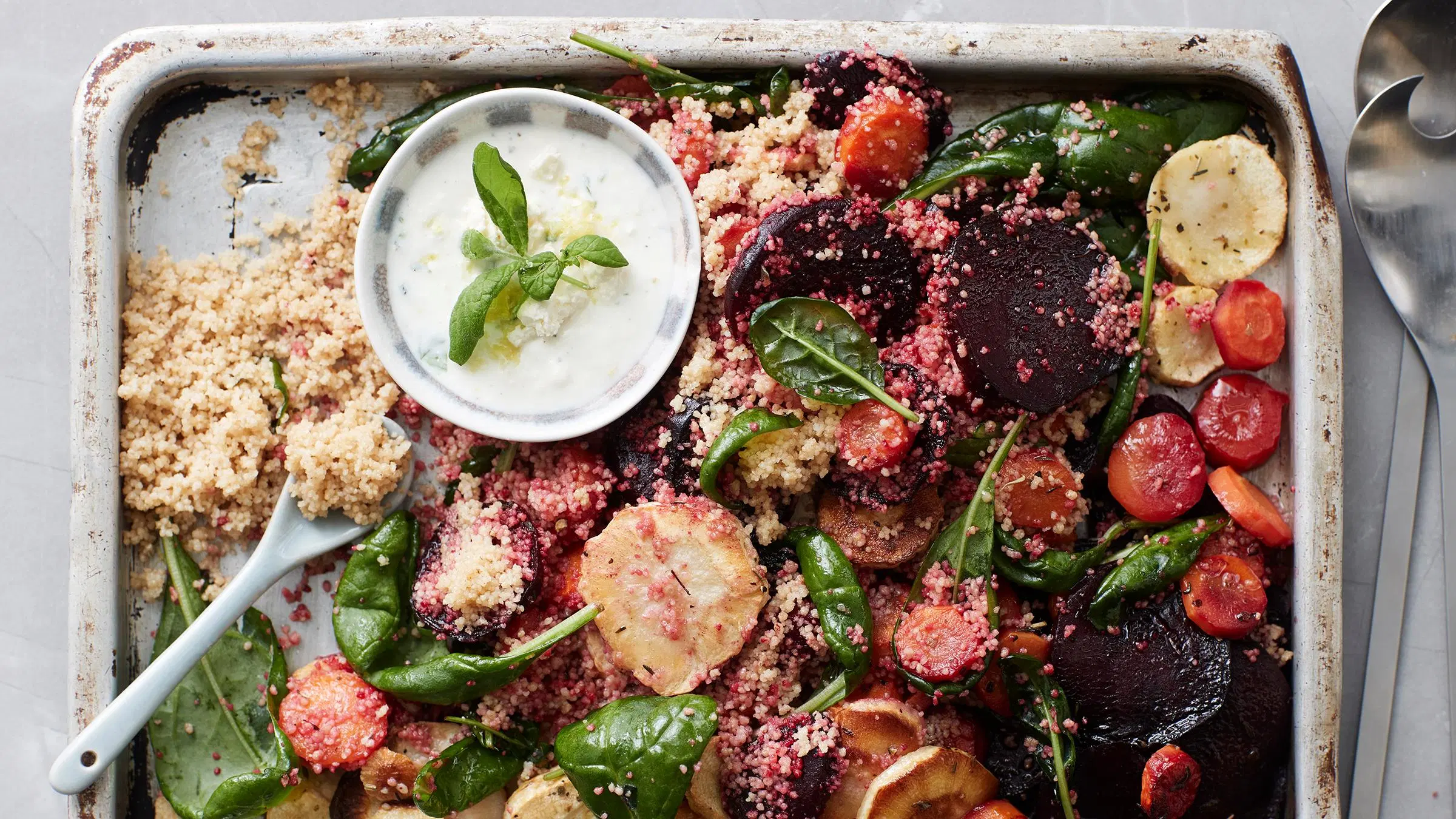 Paahdetuista juureksista, pinaatinlehdistä ja kuskusista tehty salaatti pellillä. 