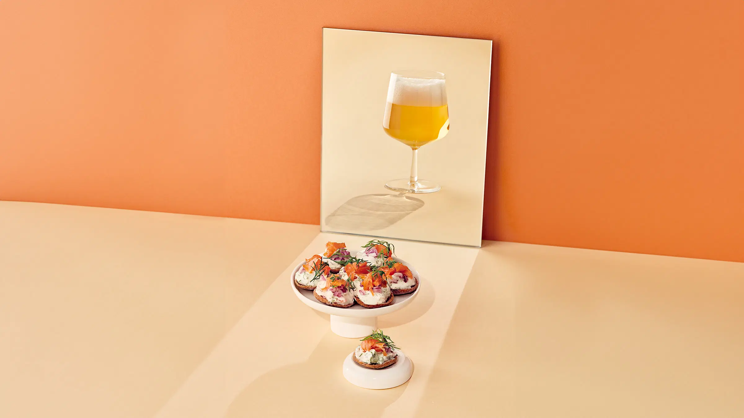 Lautasella ruisnappeja, joissa on lohimoussea. Taustalla peilistä heijastuu lasillinen olutta.