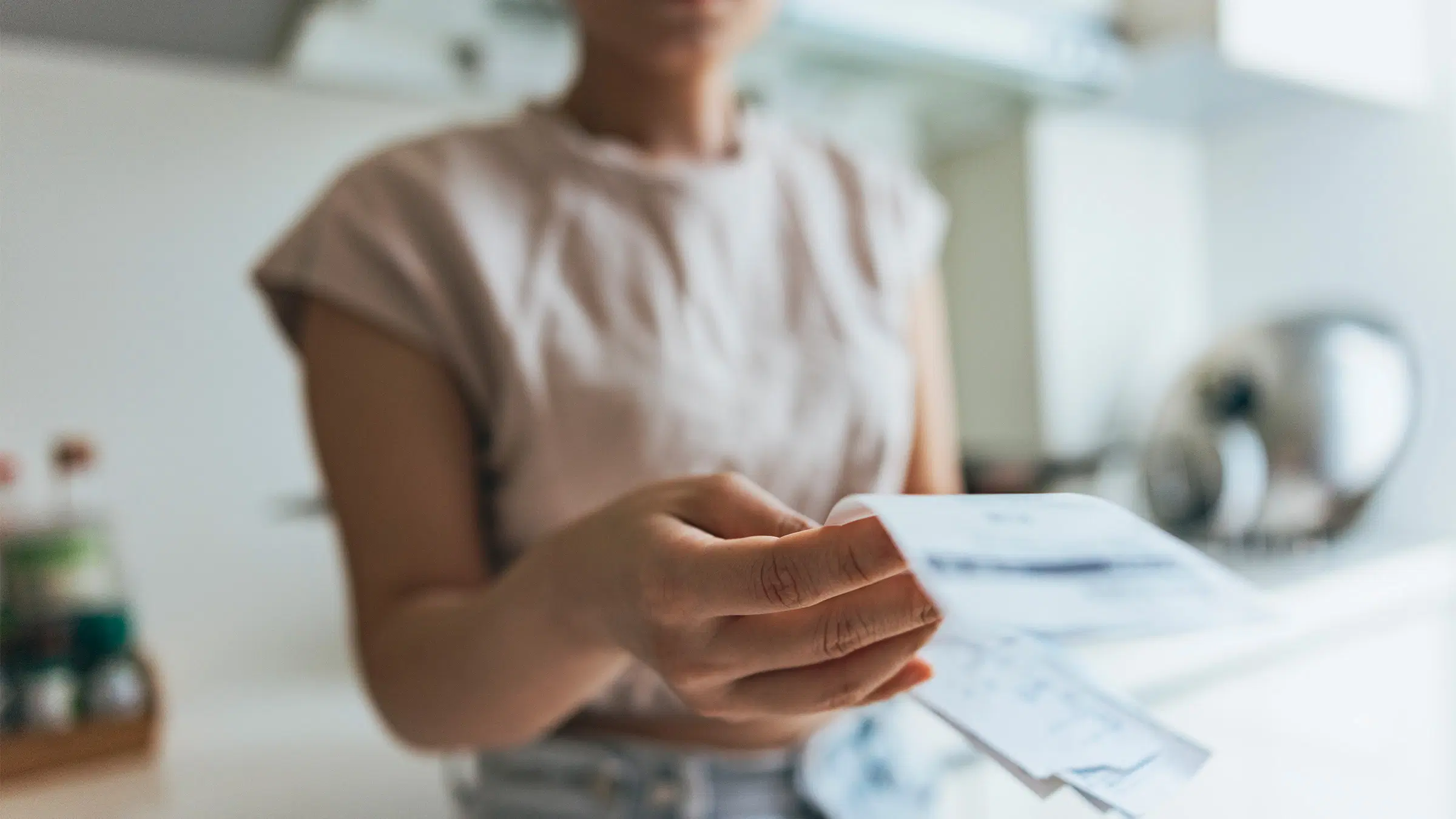 Nainen laskee säästöjään kuitista keittiössään.