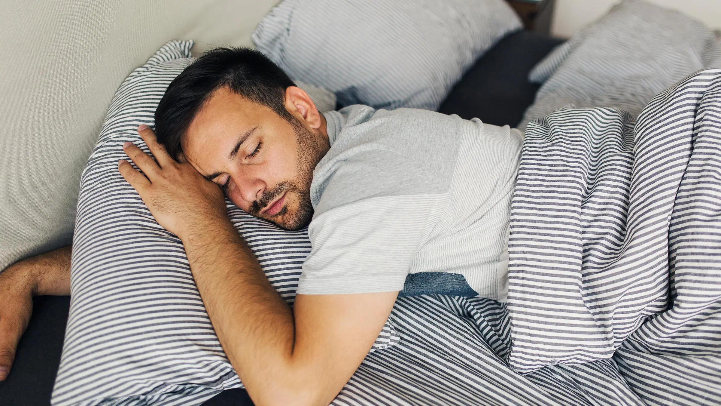 Mies nukkuu raidallisissa lakanoissa.